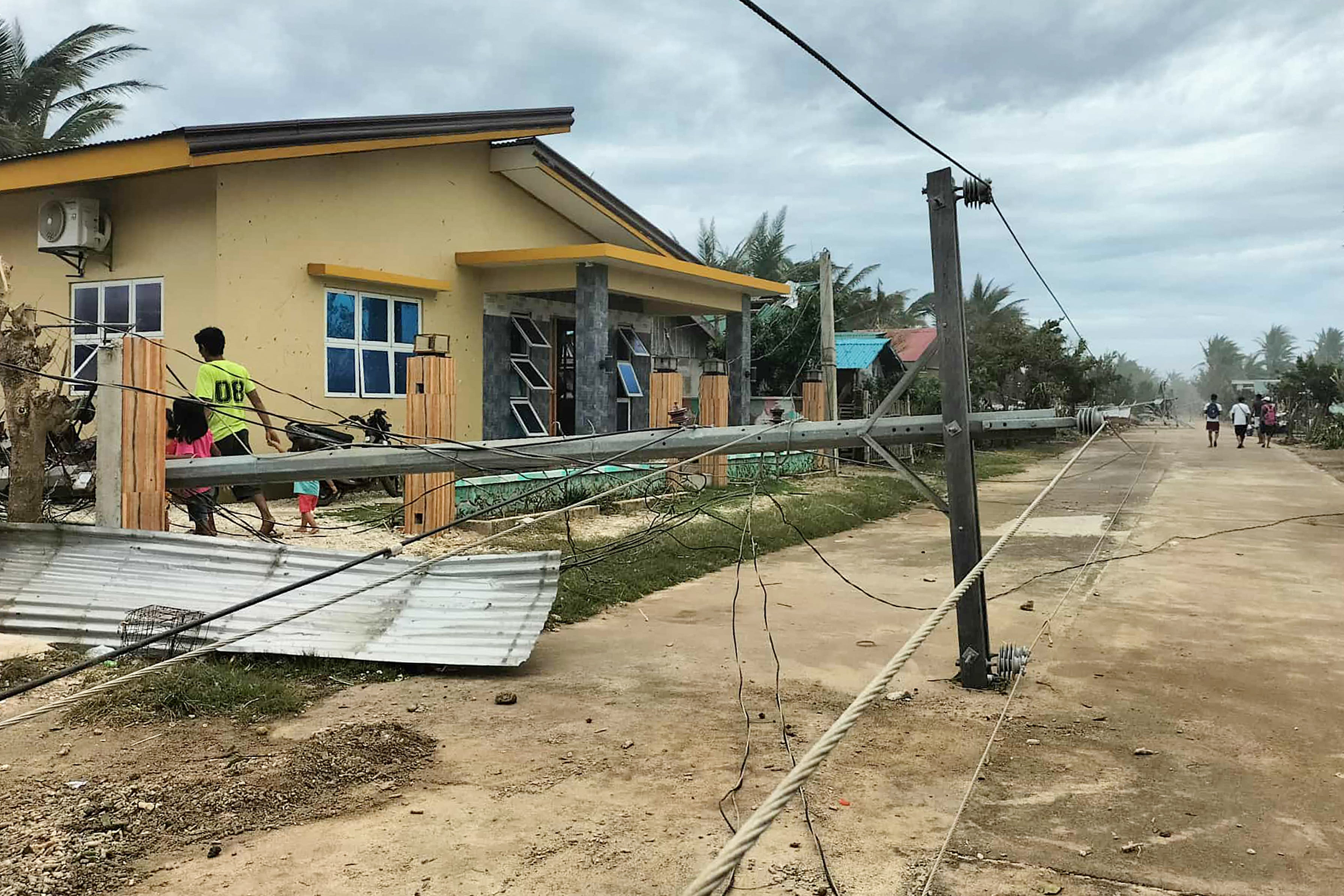Residents walk past a fallen electric post along a road in Calayan island, Cagayan province