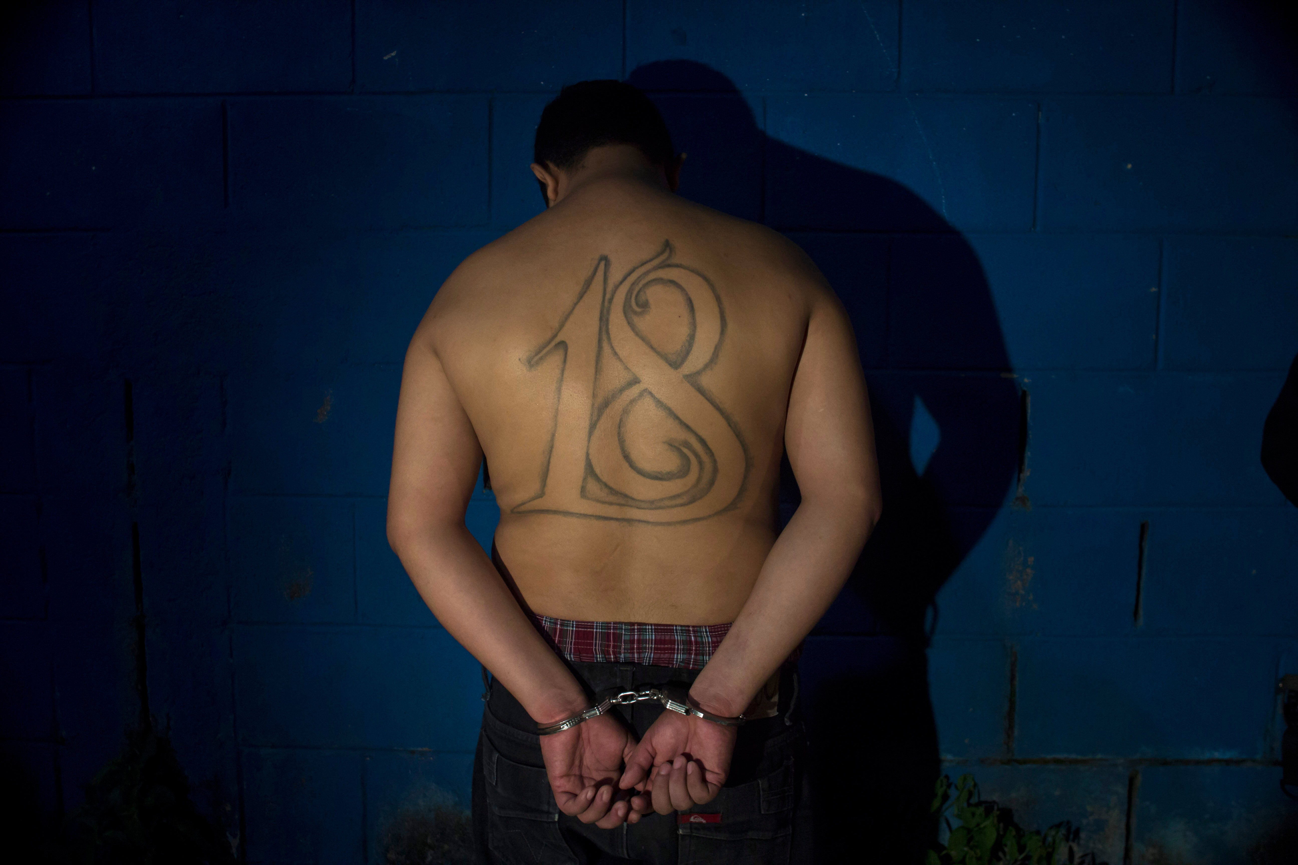 A leader of the Barrio 18 gang stands handcuffed facing a wall after his arrest in El Salvador earlier this year