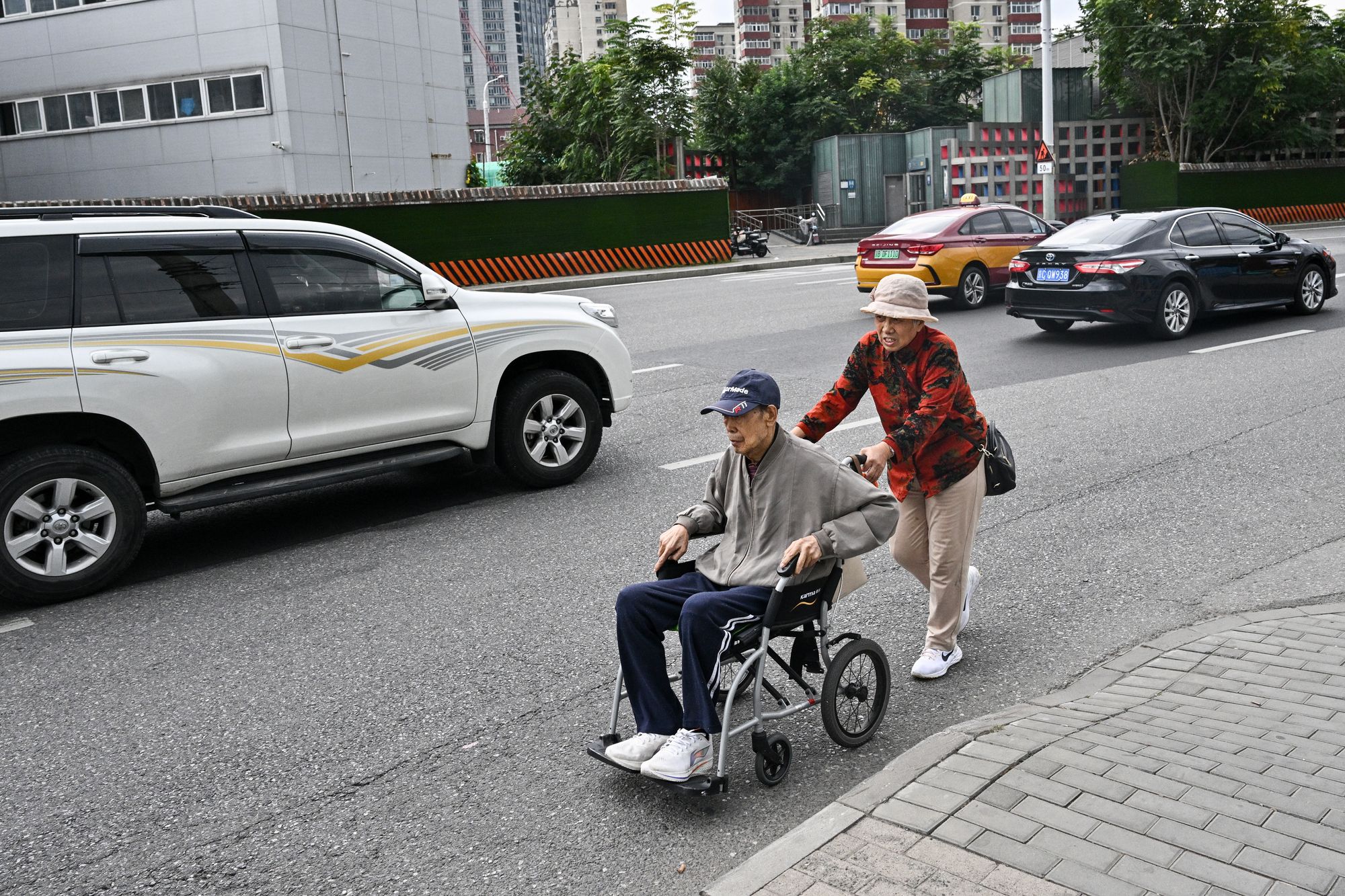 A woman pushes an elderly man in a wheelchair along a street in Beijing