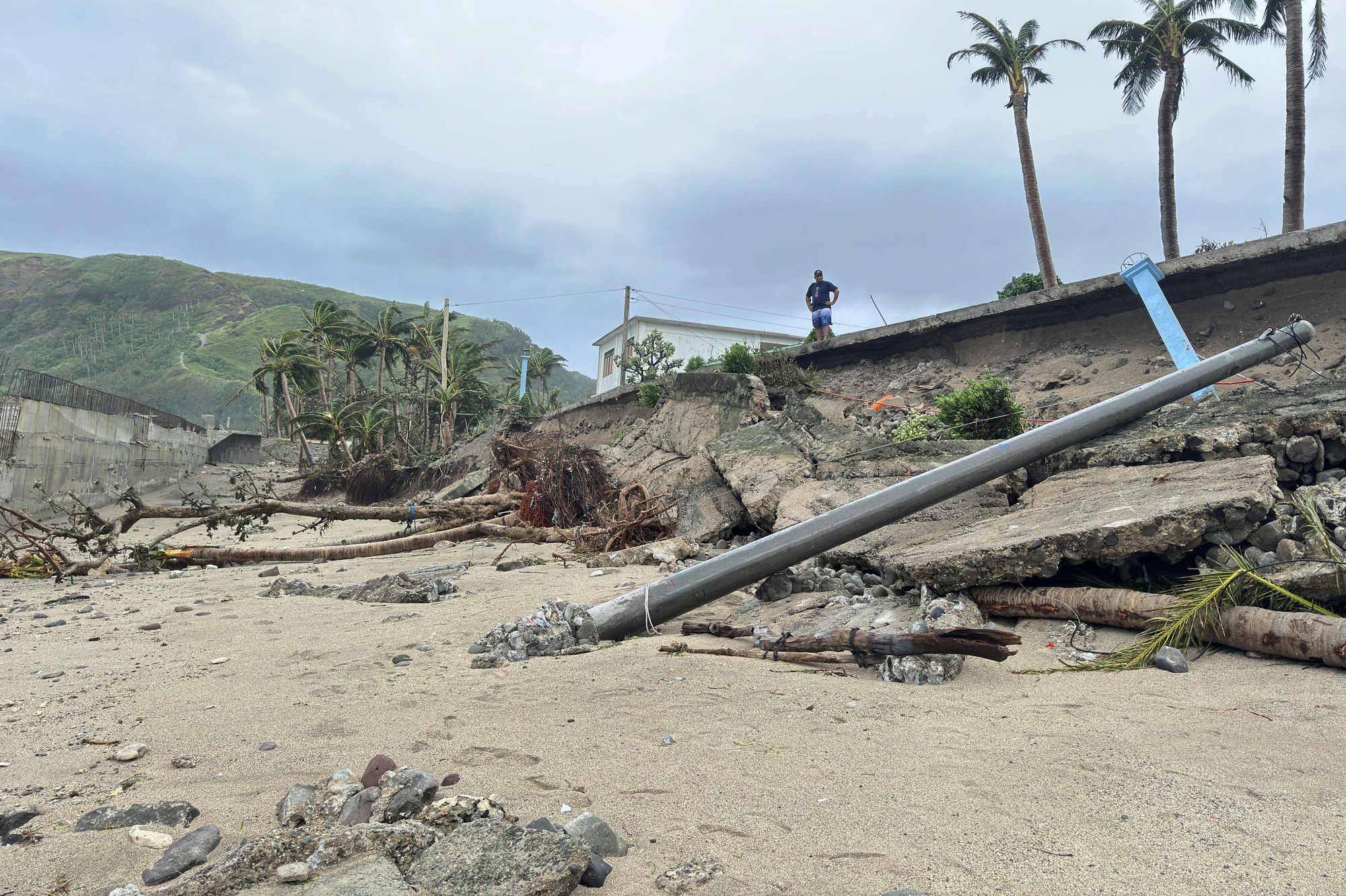 A man stands beside a damaged road due to Typhoon Ragasa in Uyugan, Batanes province, northern Philippines