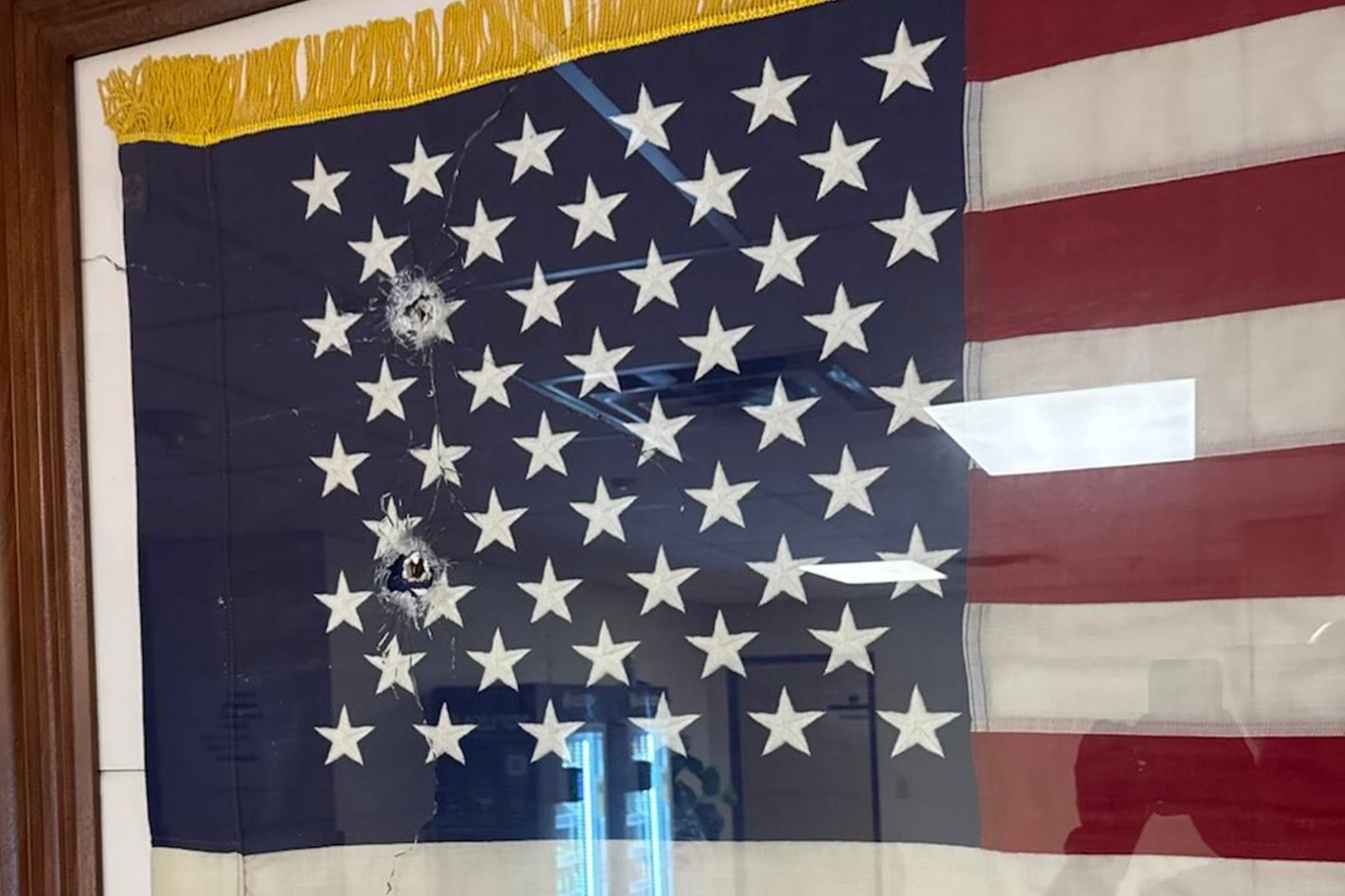Bullet holes can be seen in the glass of a framed American flag inside the Dallas, Texas ICE facility where three people were shot on Wednesday morning