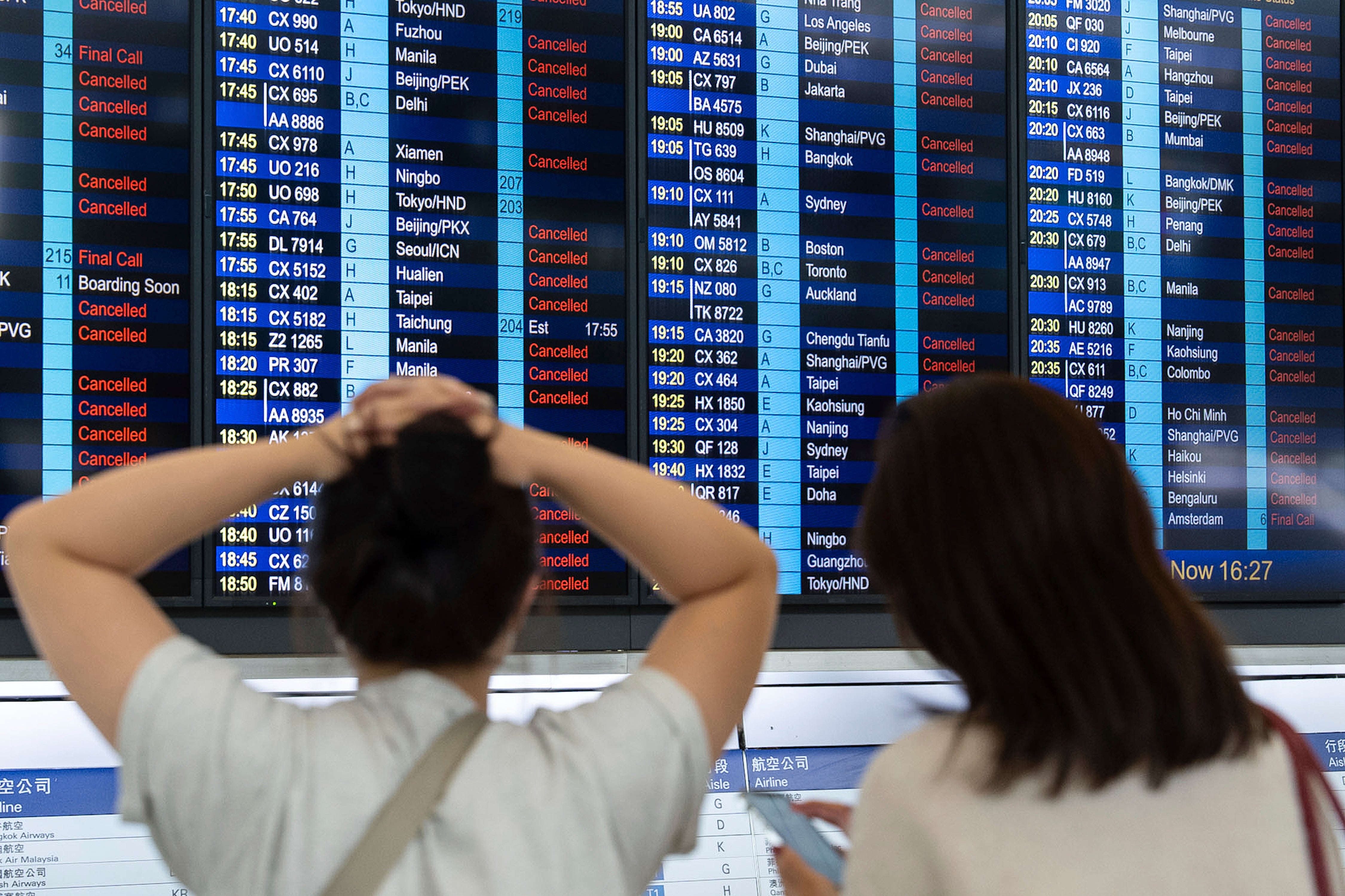 Passengers look at an information display board showing canceled flights due to the super typhoon Ragasa, at the Hong Kong International Airport