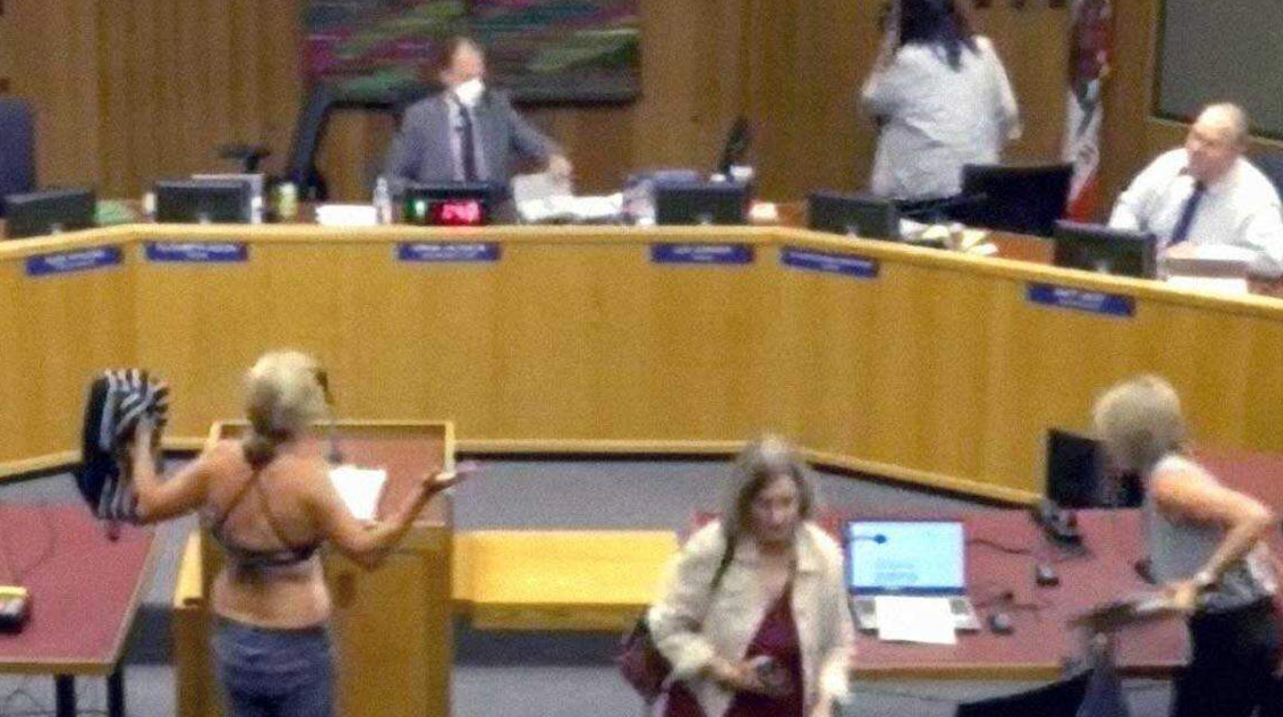 Moms for Liberty chapter chairwoman in Yolo County, California Beth Bourne, right, removes her shirt during a Davis Joint Unified School District board meeting to protest a policy allowing transgender students to choose which bathroom they use