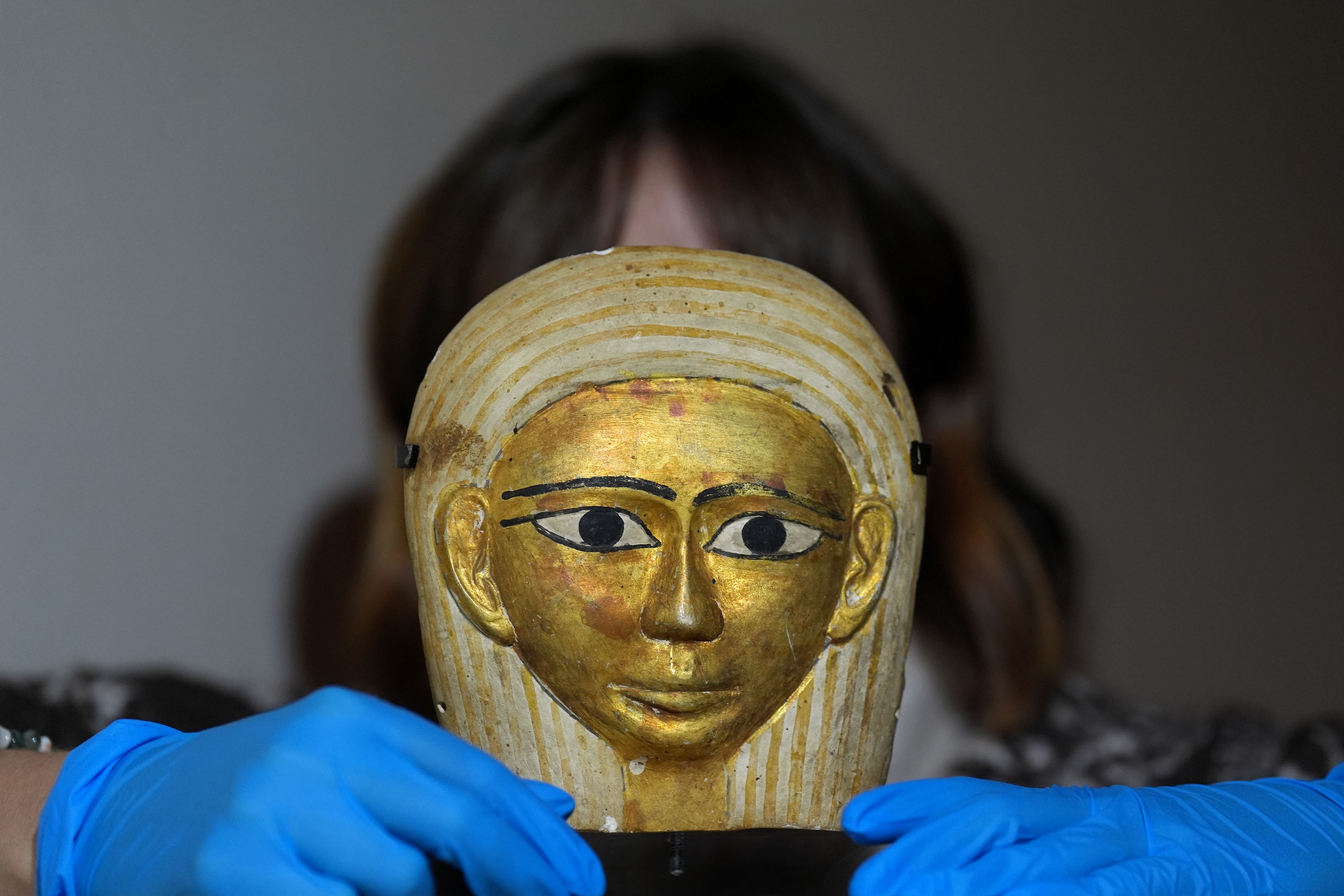 Gallery technician Tash Lawson inspects a 2,000-year-old gilded Egyptian coffin mask at the Made in Ancient Egypt exhibition (Joe Giddens/ PA)