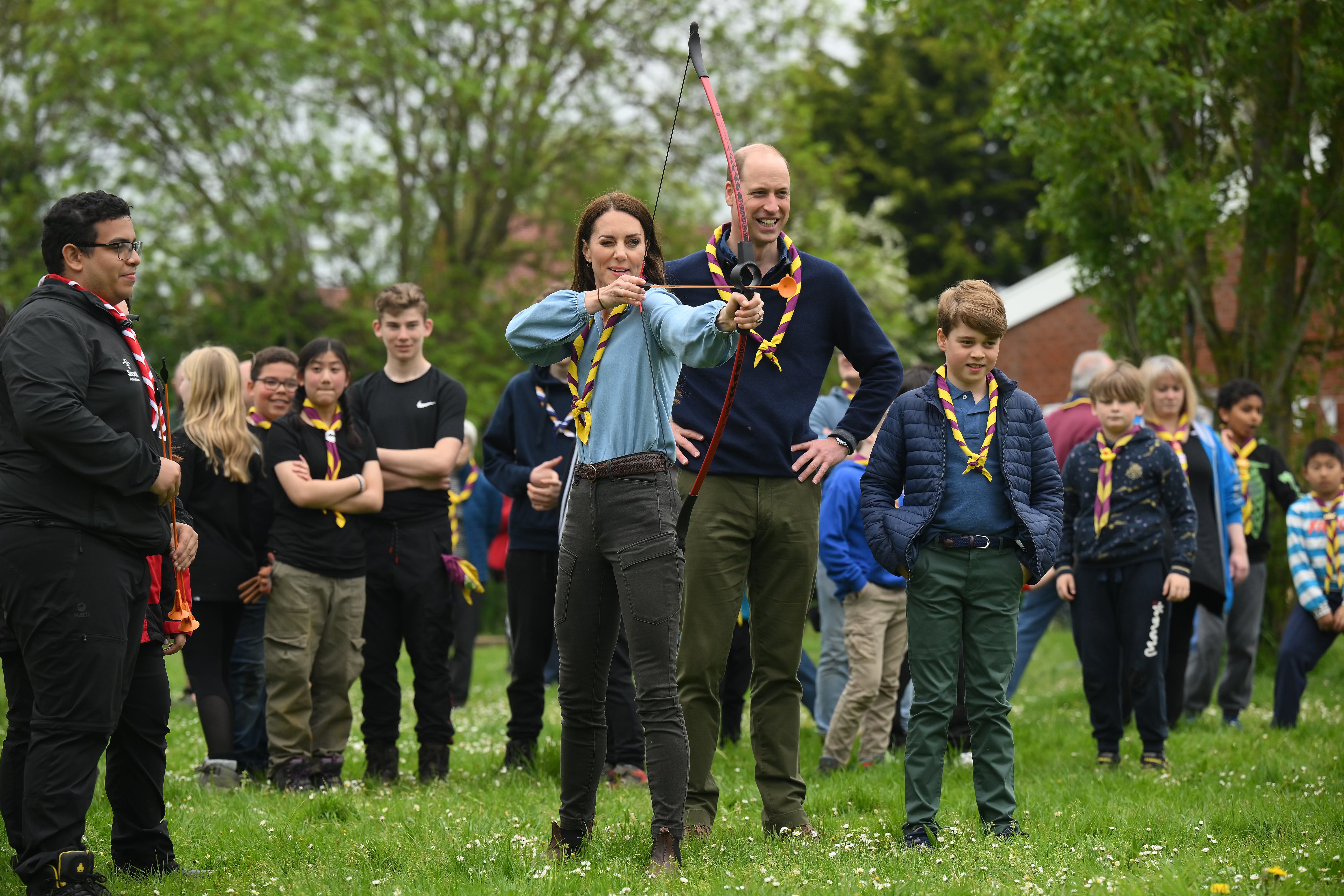 Kate, watched by William and their son, tries her hand at archery at a Scout hut in Slough