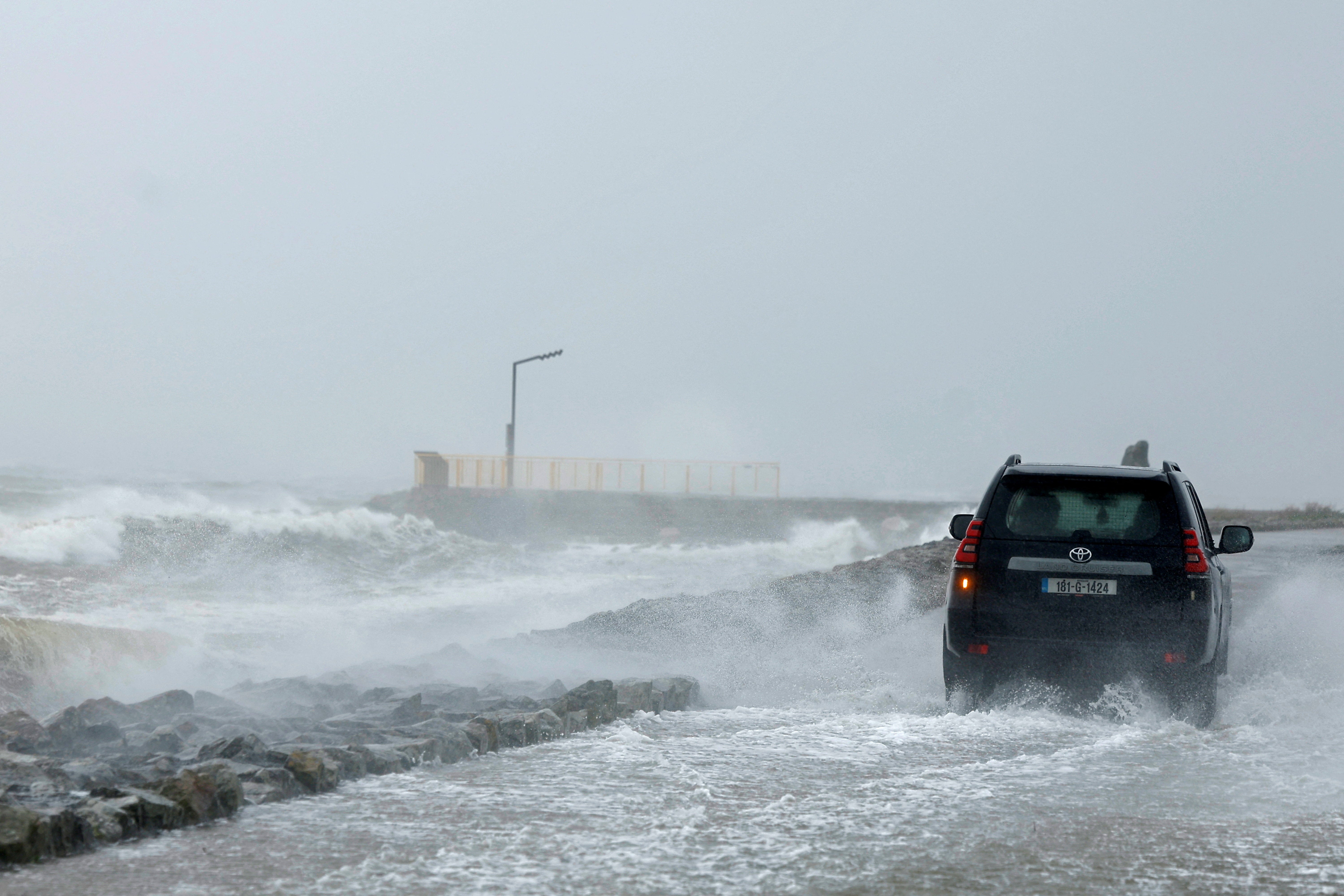 A person drives their car drives on a footpath as the road is flooded during Storm Amy which brought severe weather, in Galway, Ireland