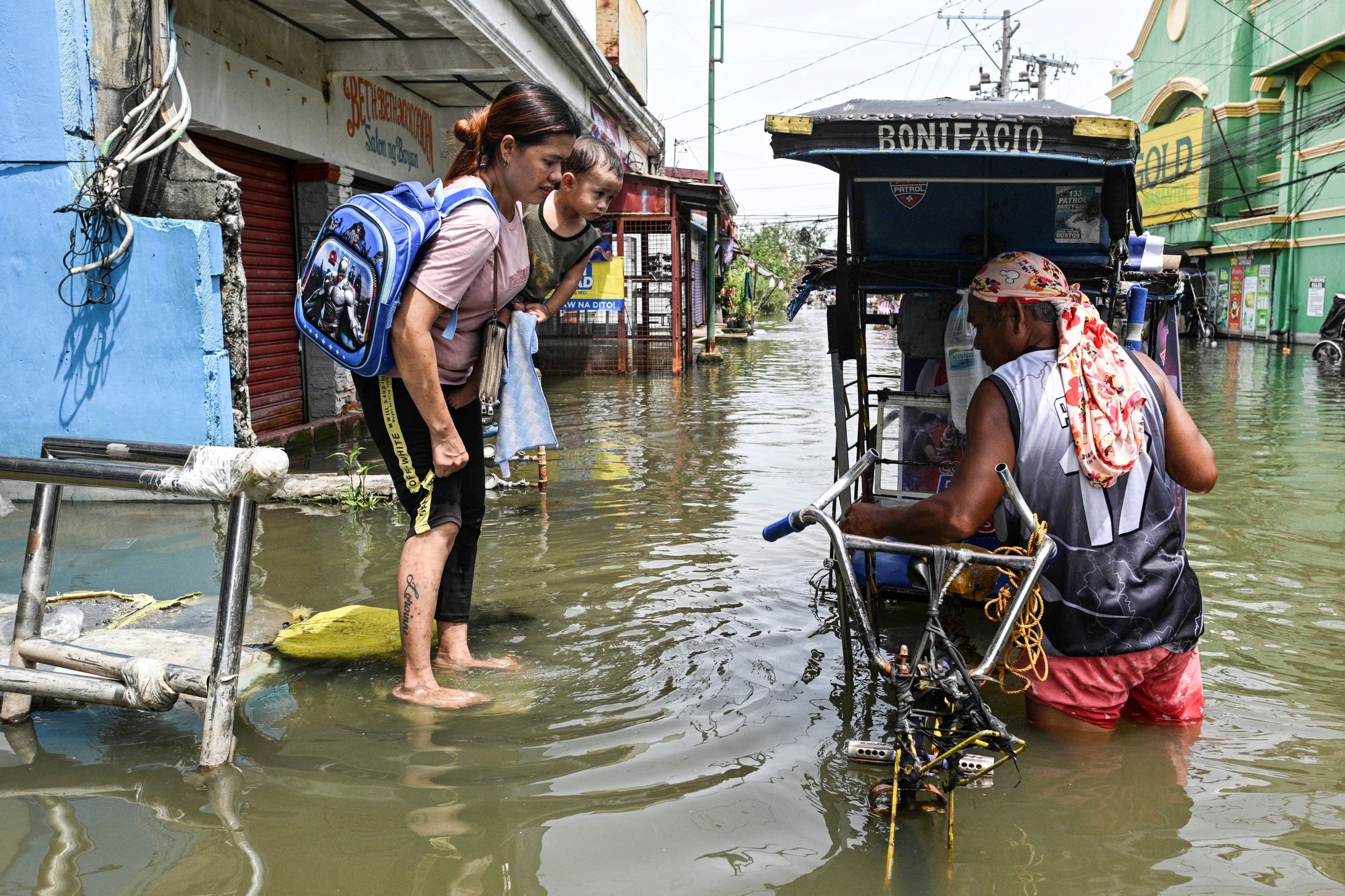 A woman carrying a baby, prepares to ride a pedicab to cross a flooded street, intensified by rain caused by Severe Tropical Storm Matmo, in San Roque, Macabebe, Pampanga, Philippines