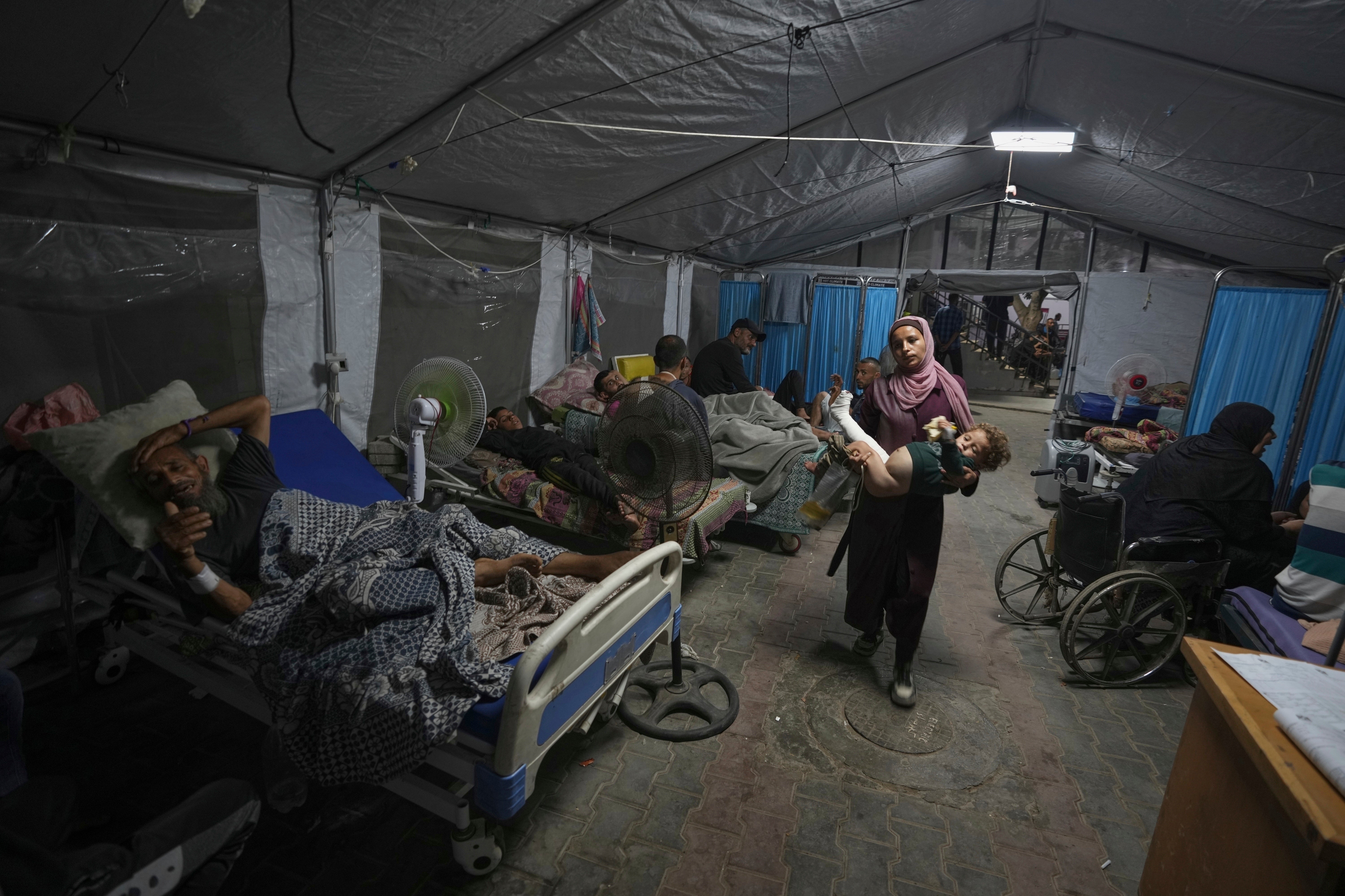 A mother carries her child into a patient treatment tent outside Shifa Hospital in Gaza City in July