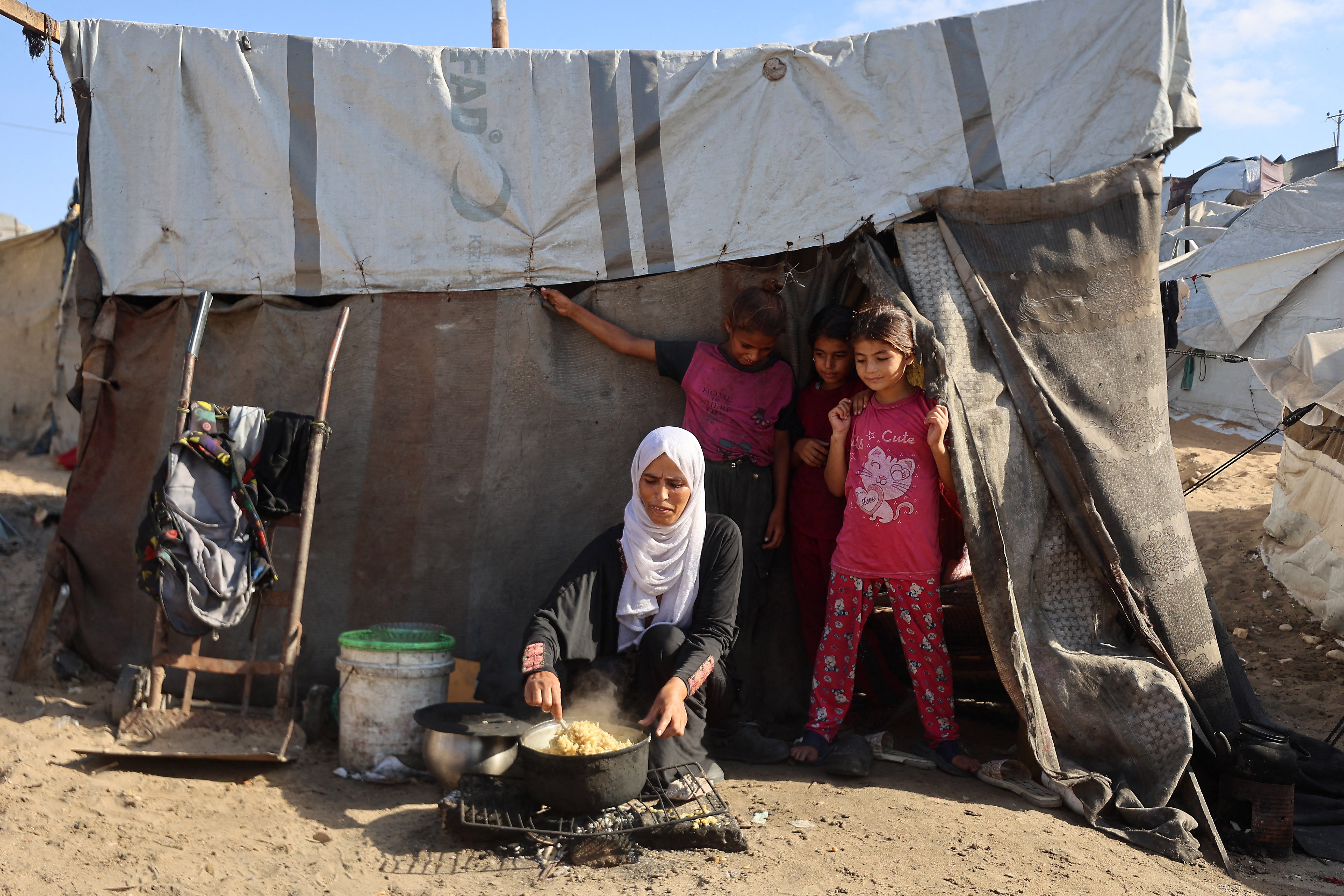 A Palestinian woman cooks next to children in front of a tent at a camp for displaced people in Khan Younis in the southern Gaza Strip, on 29 September 2025