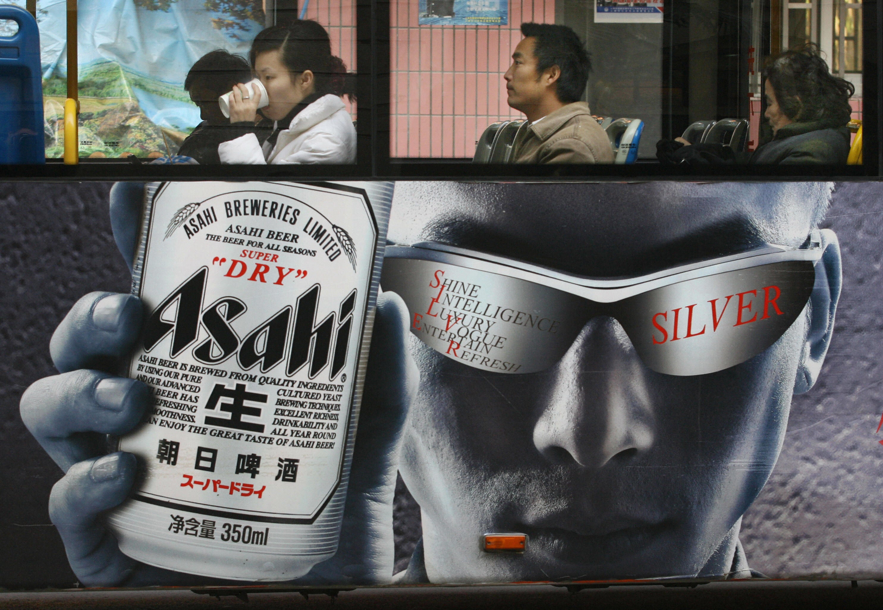 Bus passengers sit above an ad for Asahi Beer in Shanghai