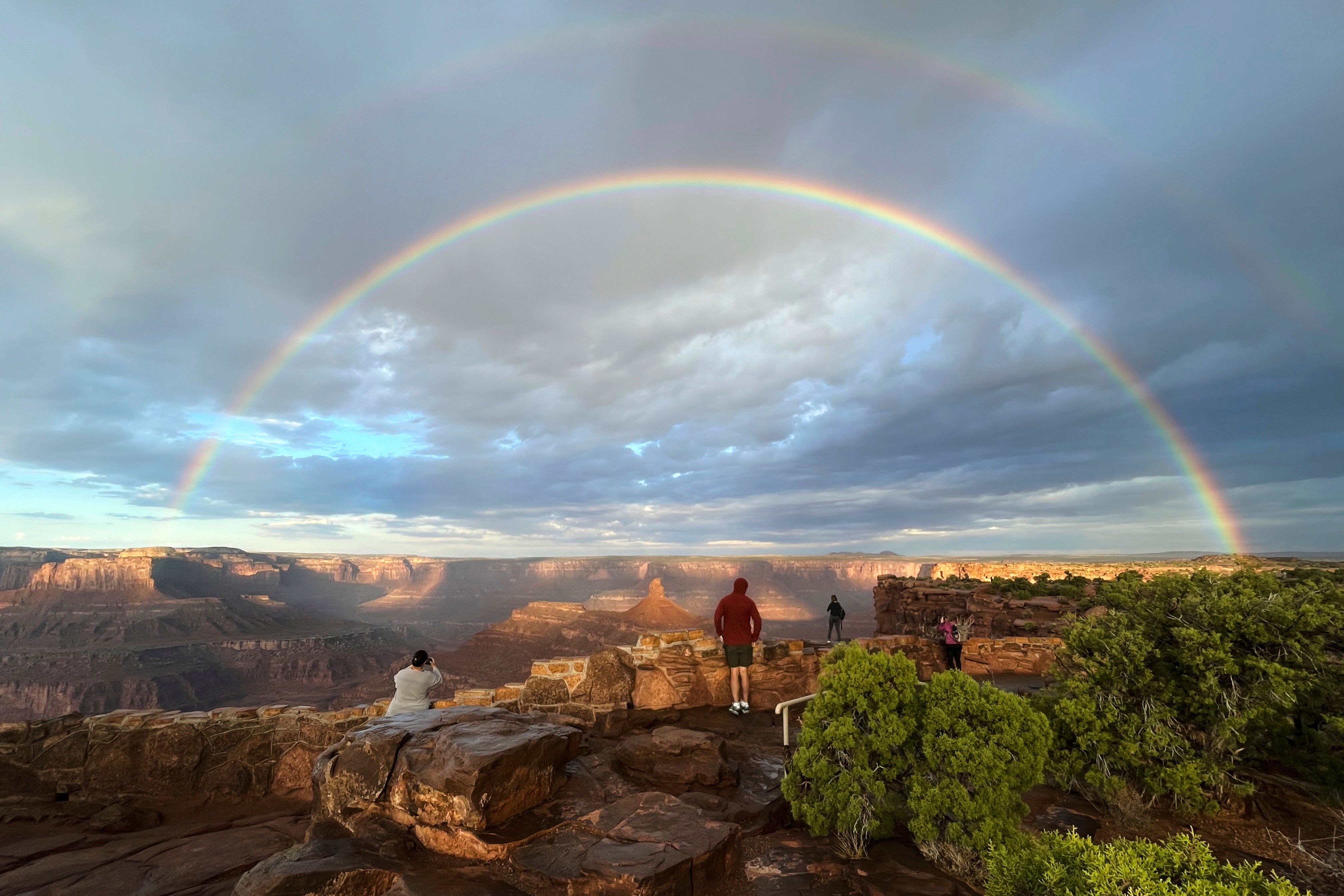 People gather at an overlook as a double rainbow appears over Dead Horse Point State Park, near Moab, Utah, after sunrise and a thunderstorm moved through