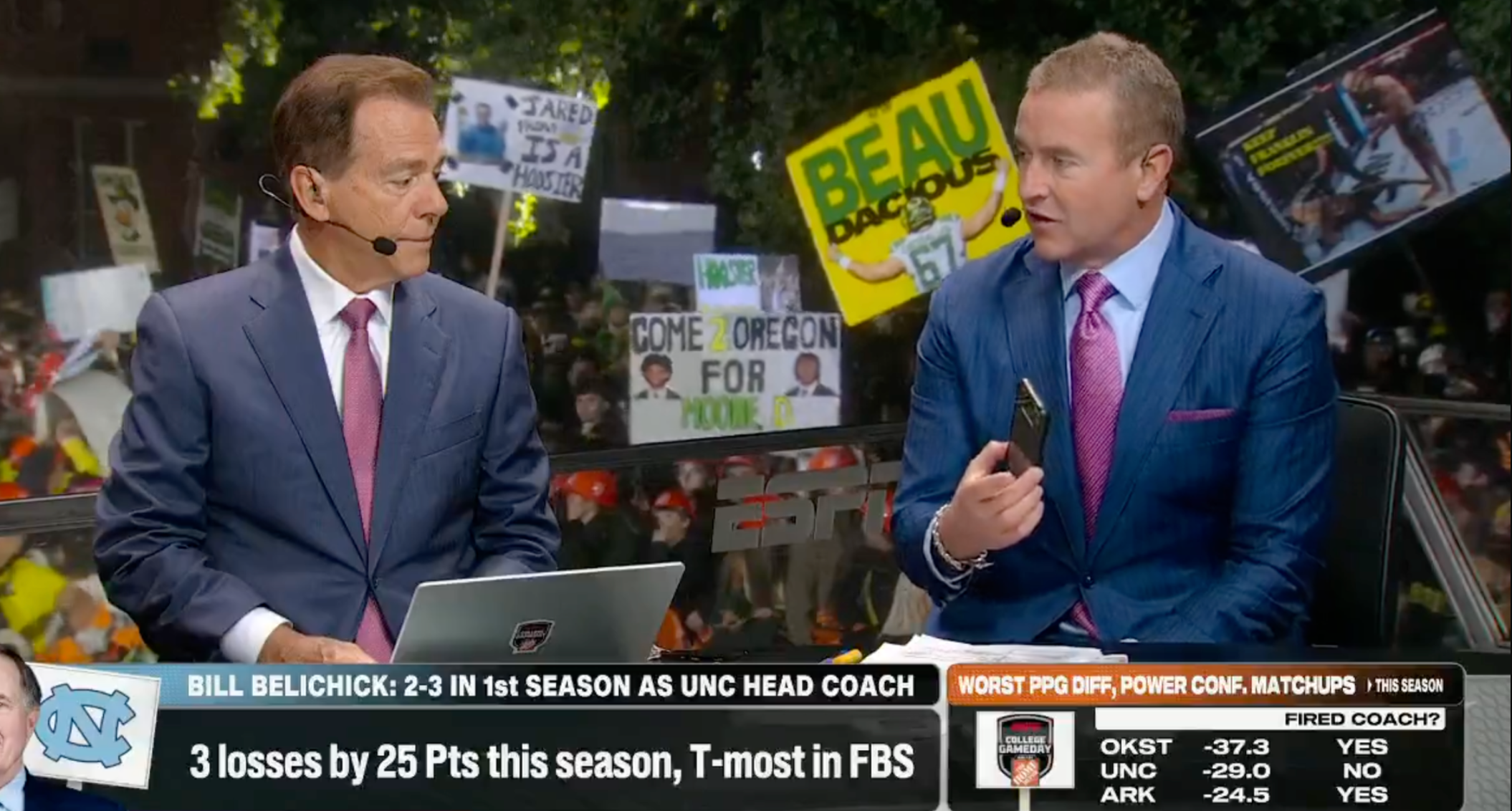 ESPN "College GameDay" host Kirk Herbstreit shows his co-host, Nick Saban, that he is receiving a call from University of North Carolina head football coach Bill Belichick during their live broadcast