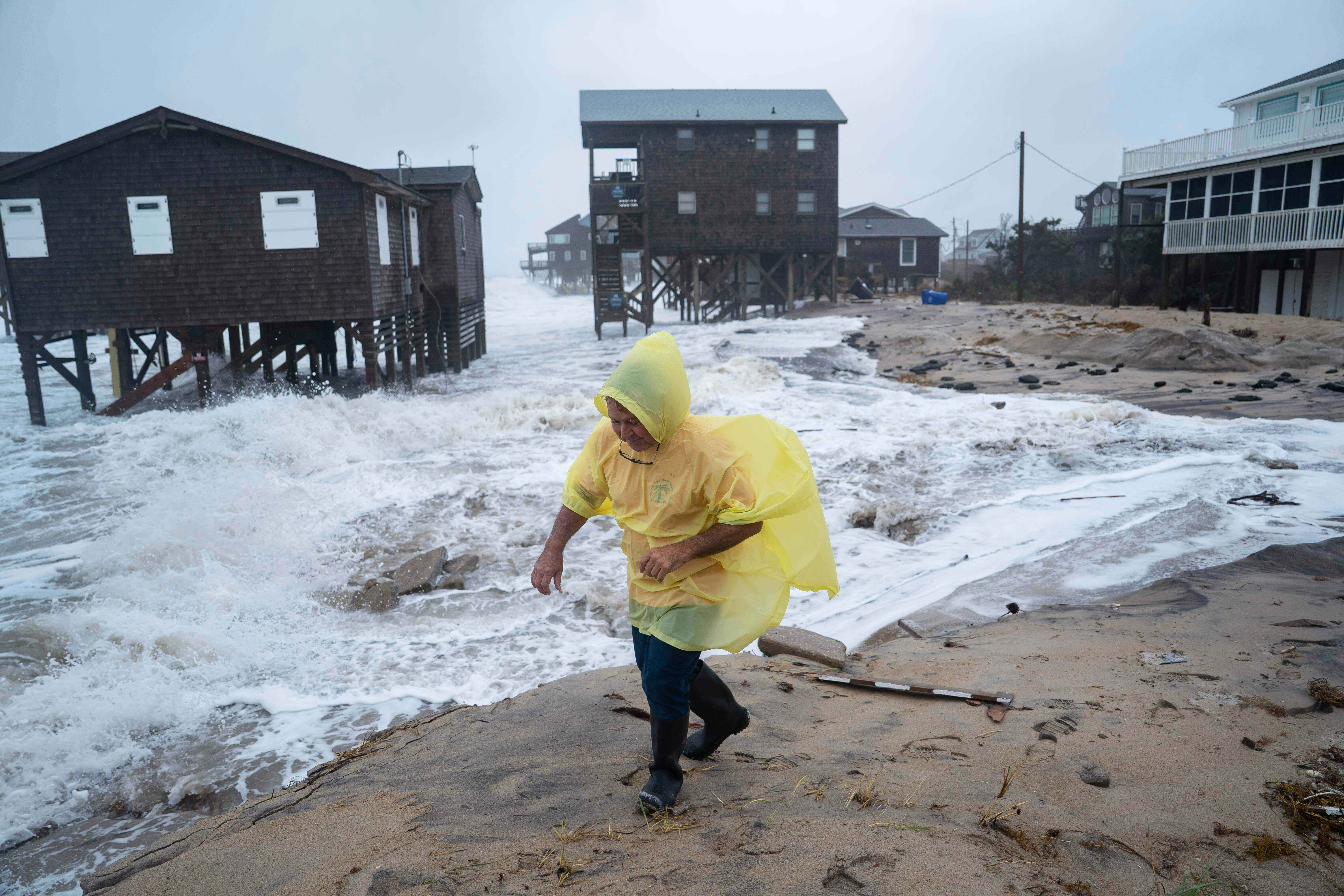 A man walks past houses at risk of collapse along the shore in the middle of the Nor’easter in North Carolina