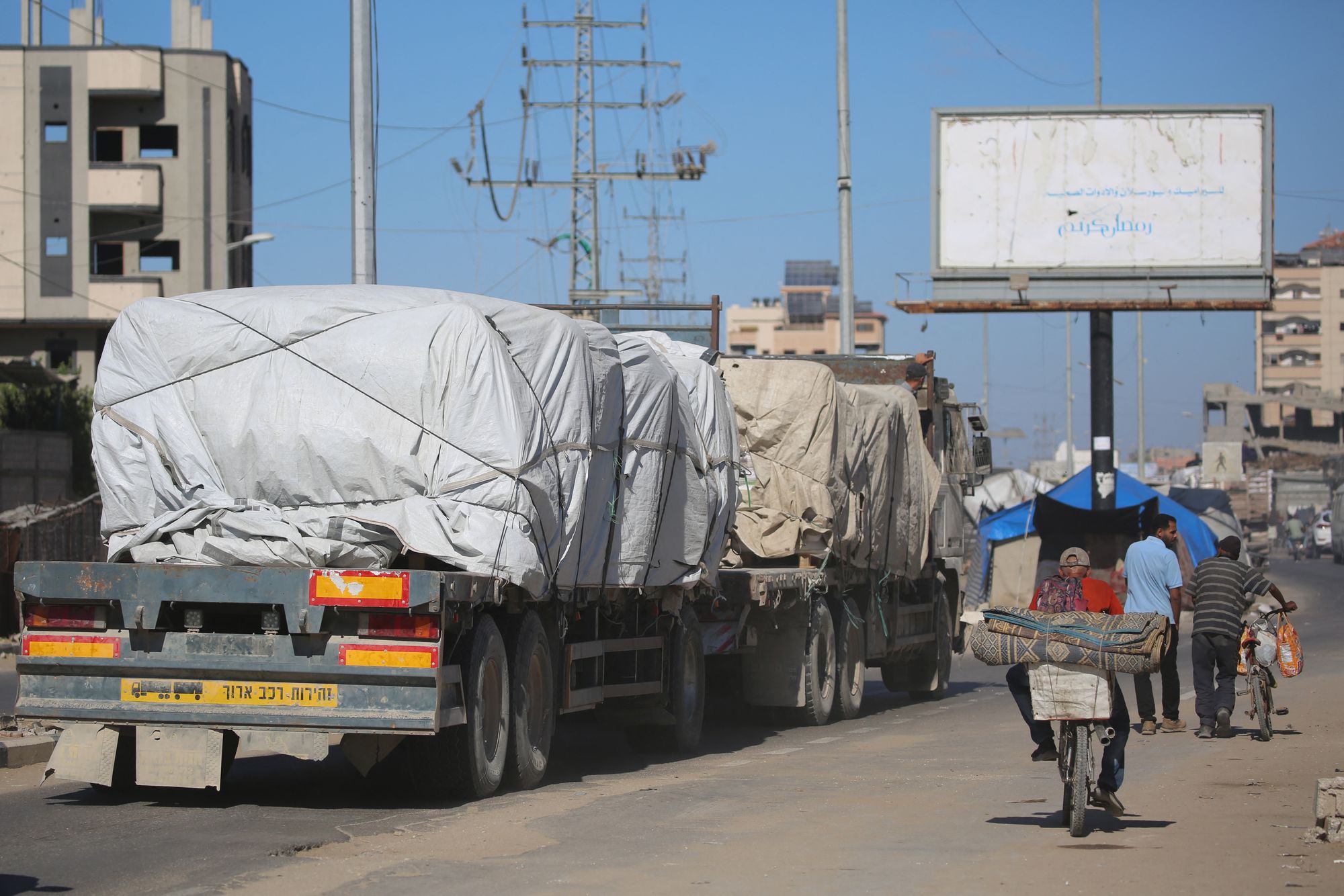 Trucks carrying aid which entered the Gaza Strip through the Karm Abu Salem crossing, drive past displacement tents at the Nuseirat refugee camp in the central Gaza Strip