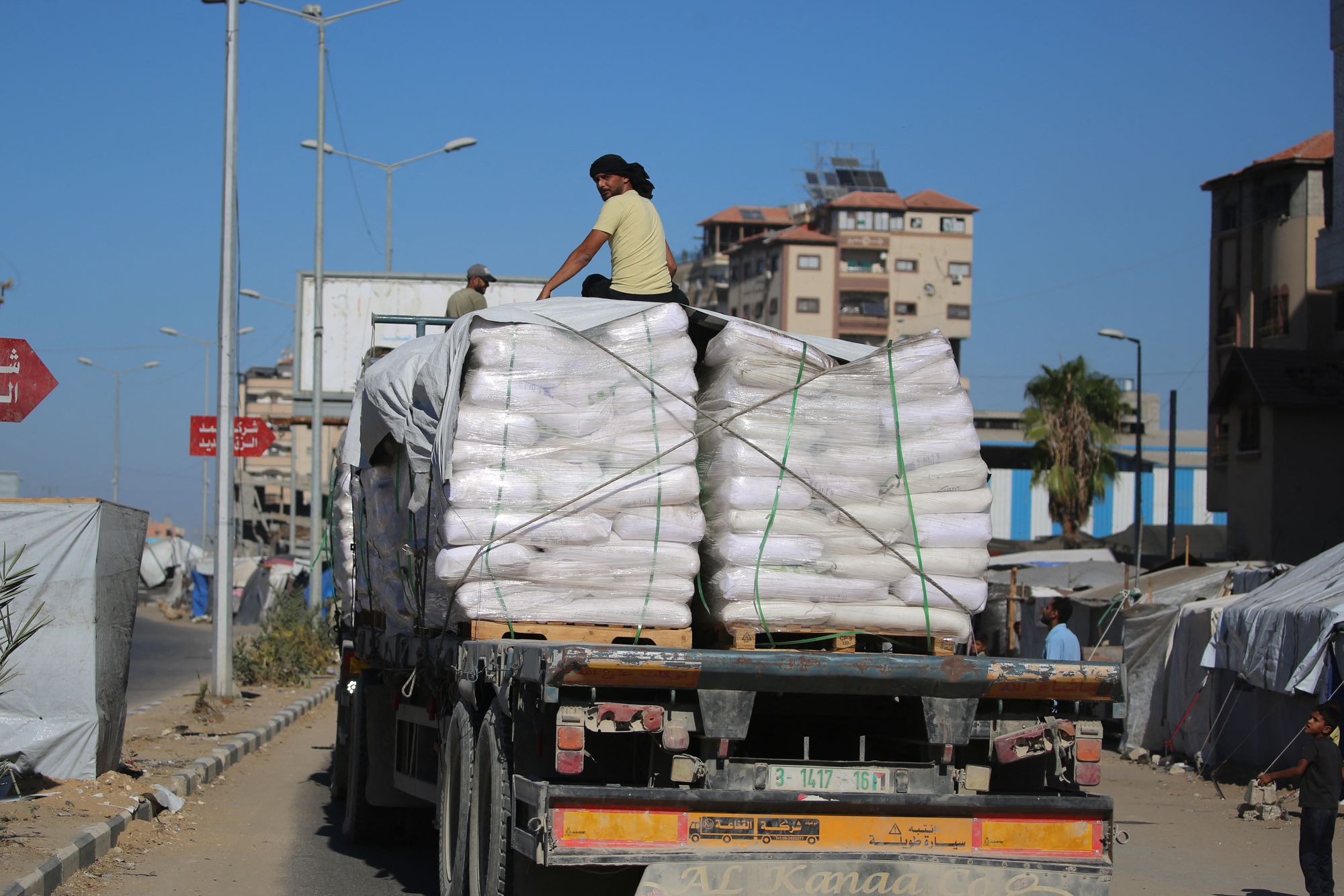 Trucks carrying aid, which entered the Gaza Strip through the Karm Abu Salem crossing, drive past displacement tents at the Nuseirat refugee camp in the central Gaza Strip on 14 October