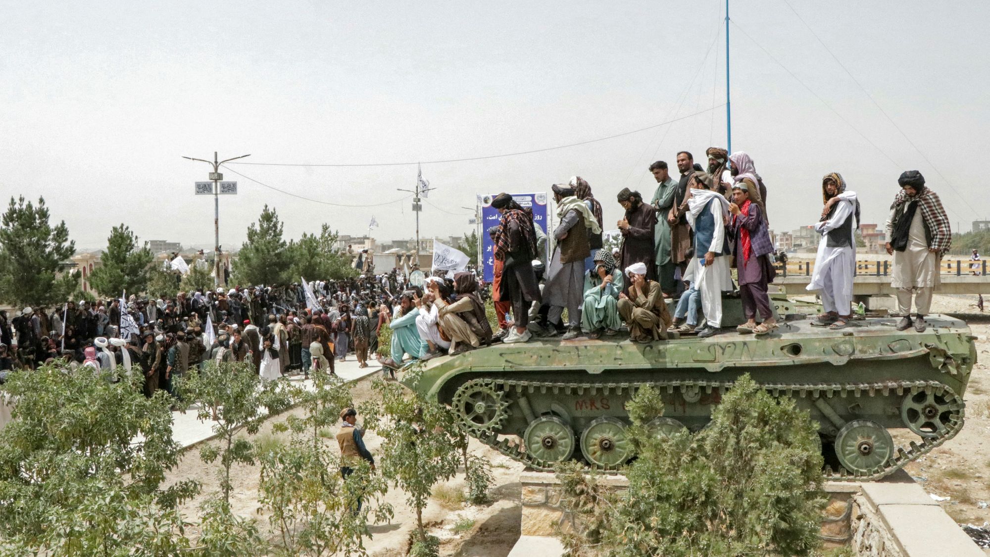 Afghan men stand over a Soviet-era tank as Taliban security personnel march during a rally in August this year