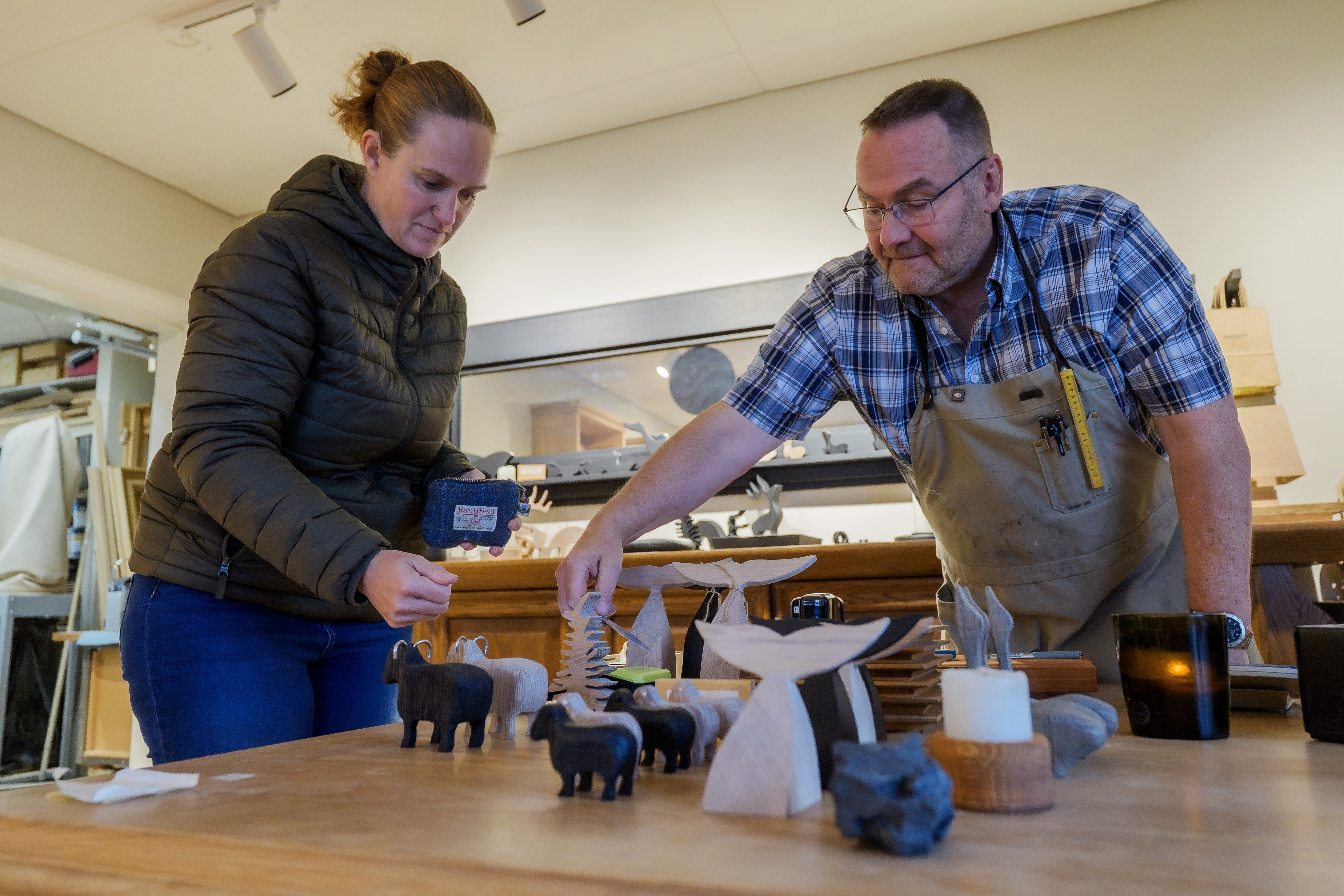 Craftsman Vignir Kristinsson helps a visitor choose among wooden sculptures in his shop in Grindavik, Iceland, Friday, Oct. 10, 2025. (AP Photo/Marco di Marco)