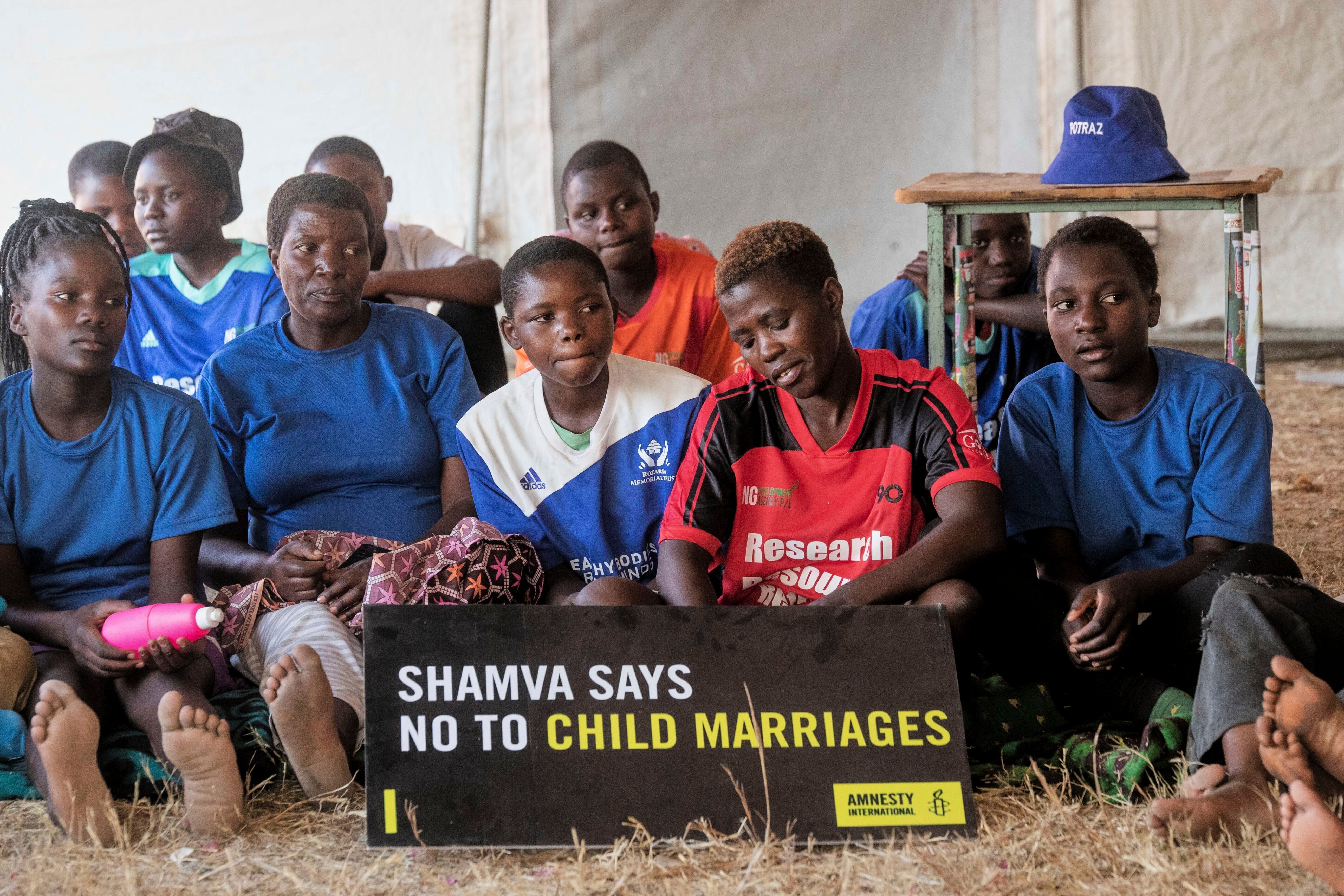 Girls and women sit inside a tent as they listen to their mentor speaking to them about child marriages at a school in Shamva, Zimbabwe, Friday, Aug. 29, 2025. (AP Photo/Aaron Ufumeli)