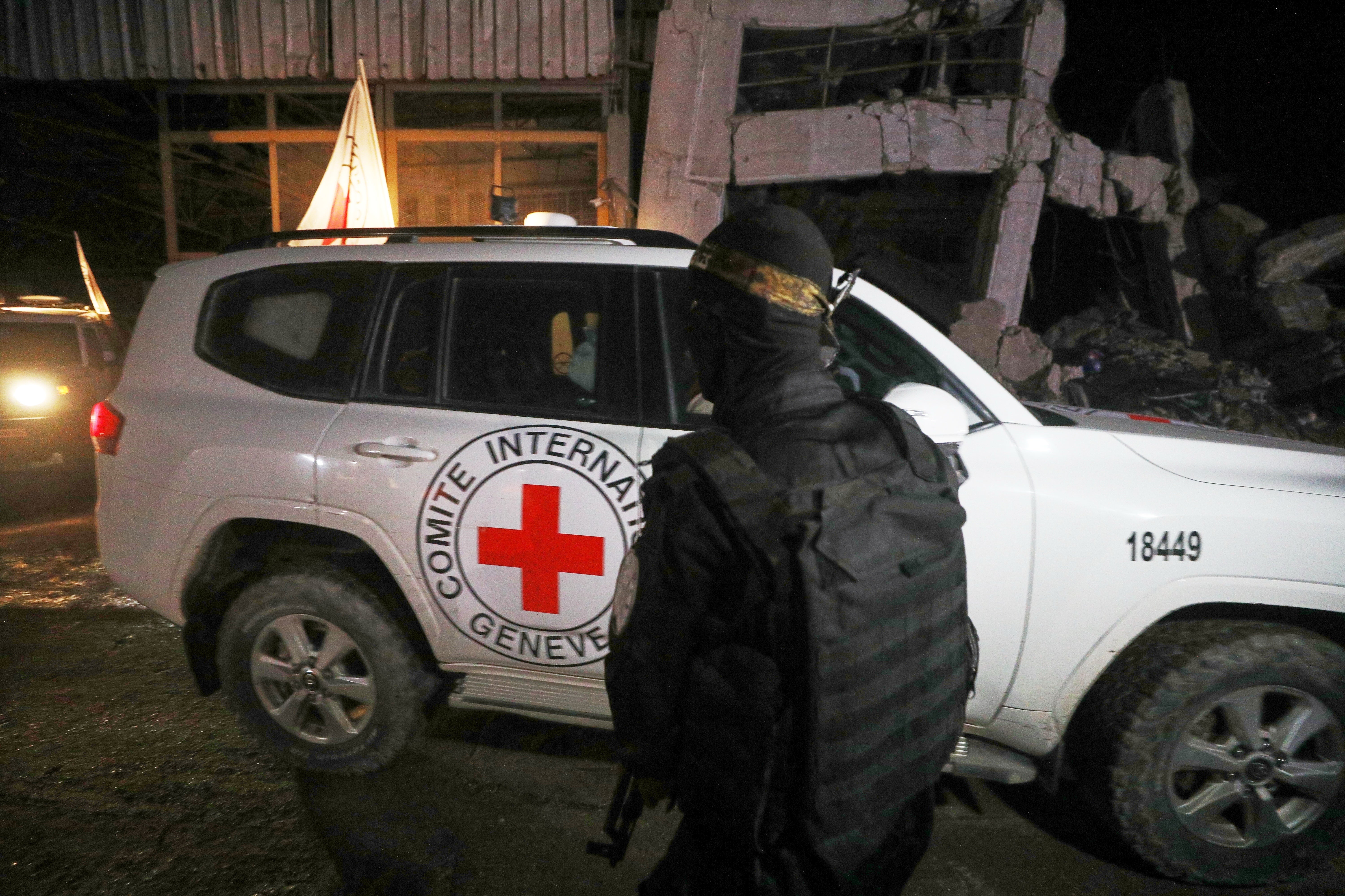 A gunman wearing the uniform of the al-Qassam Brigades, the military wing of Hamas, stands guard as Red Cross vehicles allegedly transporting coffins containing the bodies of four deceased hostages leave a warehouse for Israel, in Gaza City, Tuesday, Oct. 14, 2025. (AP Photo/Yousef Al Zanoun)
