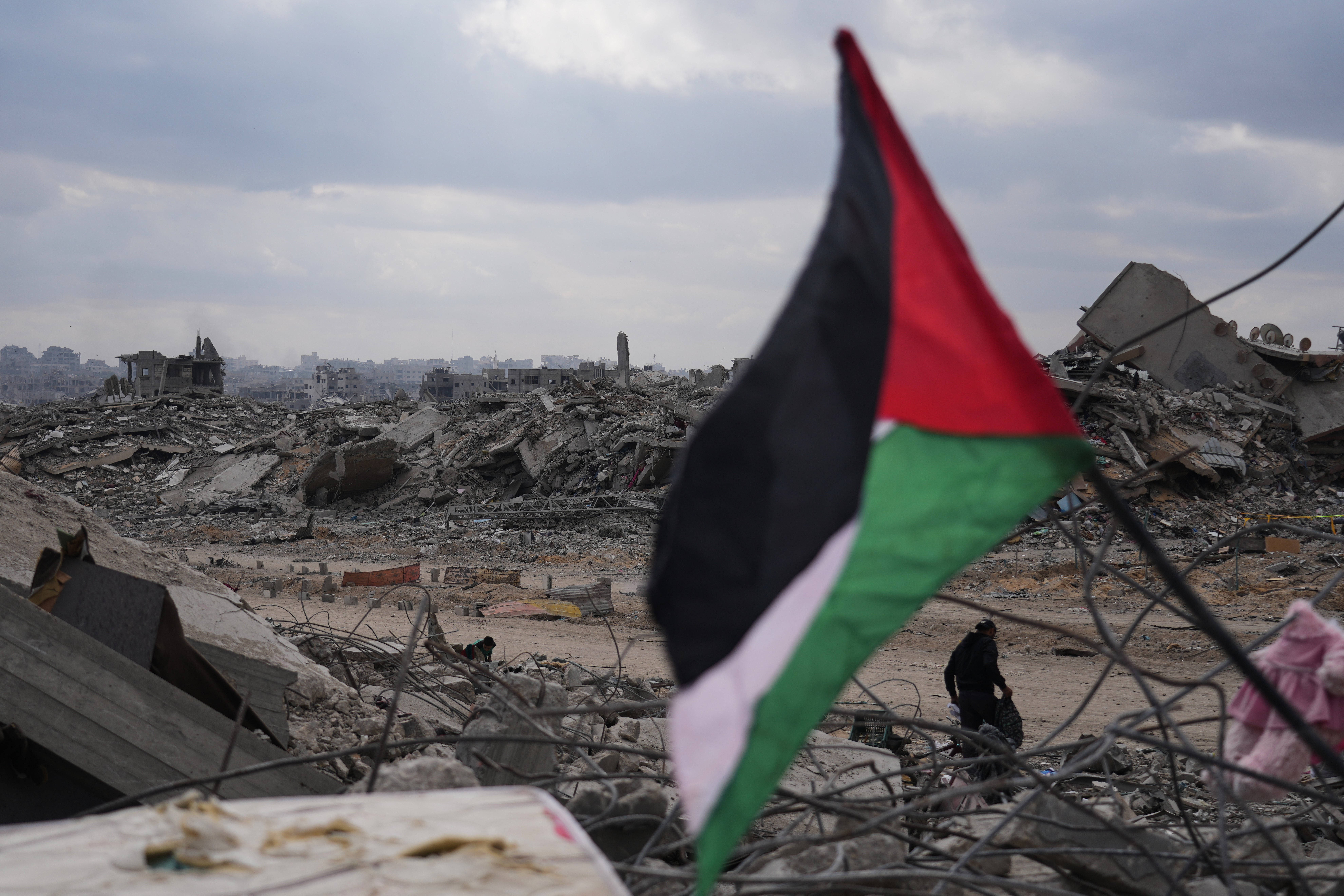 A displaced man walks past a Palestinian flag placed over the rubble of destroyed buildings in Gaza City, Sunday, Oct. 12, 2025