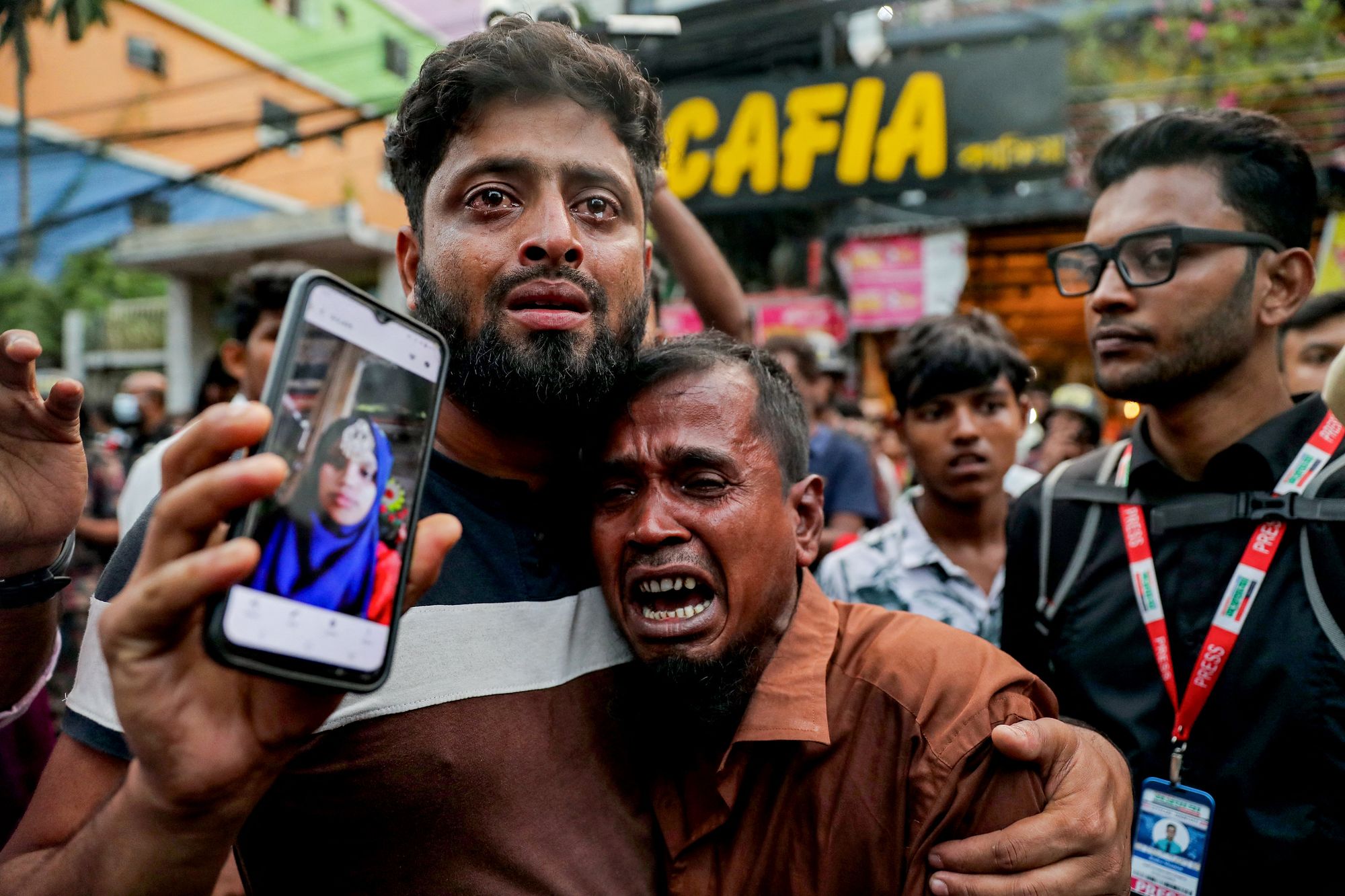 A relative wails as he shows a picture of a fire accident victim in Dhaka on 14 October 2025