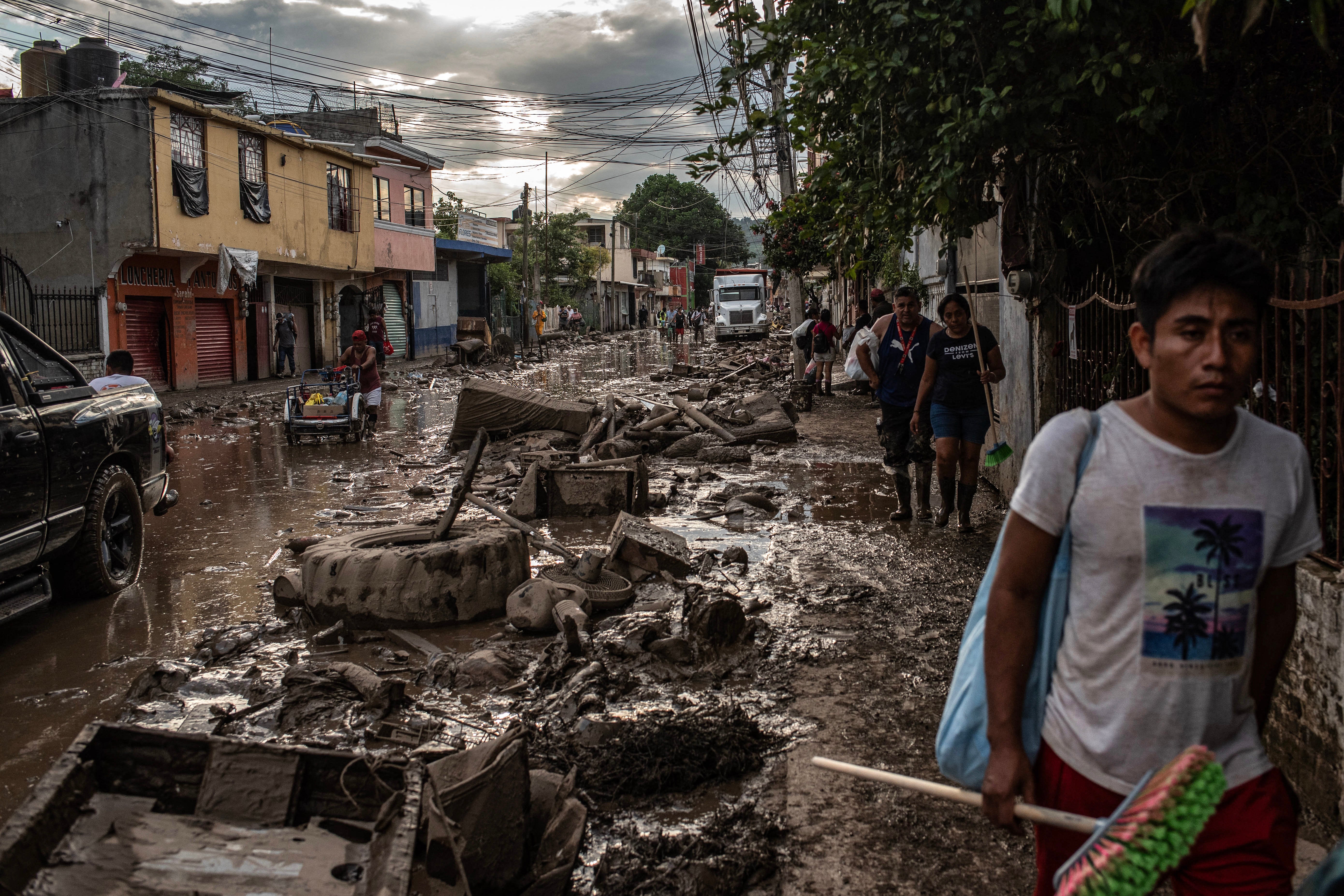 People walk past a street covered in mud and debris caused by heavy rains in the Las Granjas neighborhood in Poza Rica, Veracruz state, Mexico