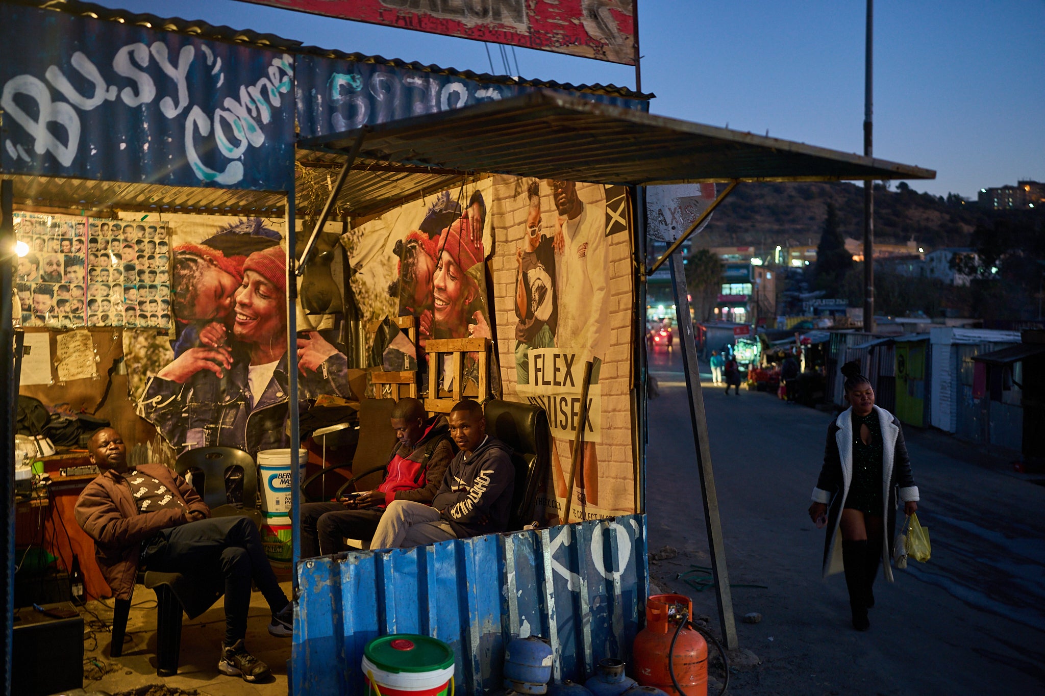 A woman passes a barber shop with men sitting inside at the end of the day in Maseru, Lesotho, July 18, 2025. (AP Photo/Bram Janssen)