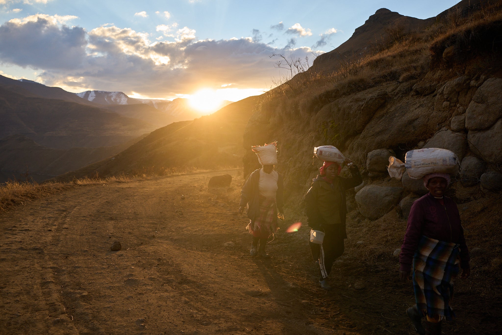 Women carry bags of food in the mountains of Ha Lejone, Lesotho, July 14, 2025. (AP Photo/Bram Janssen)