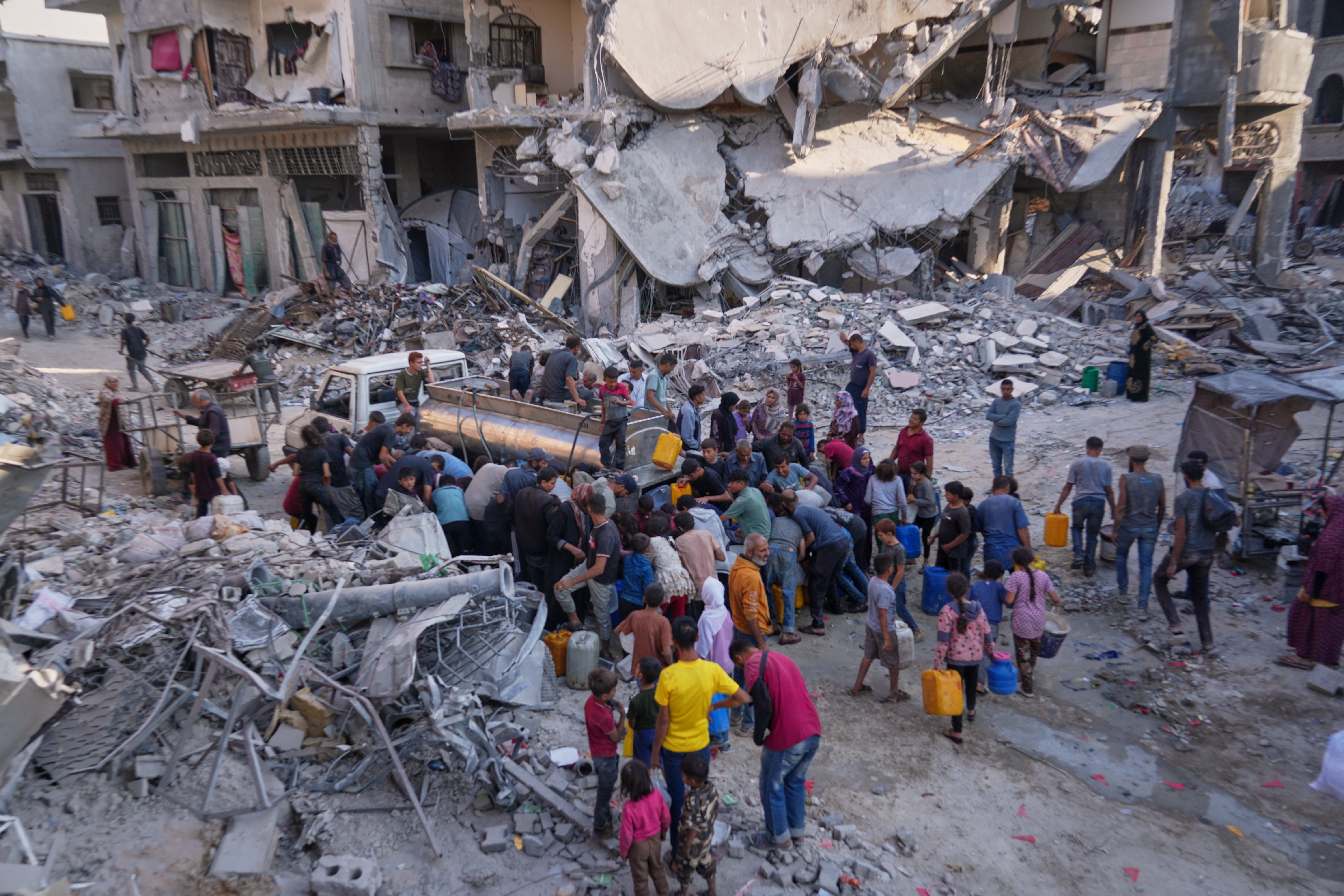 Palestinians collect water from a truck amid the destruction caused by the Israeli air and ground offensive in Gaza City
