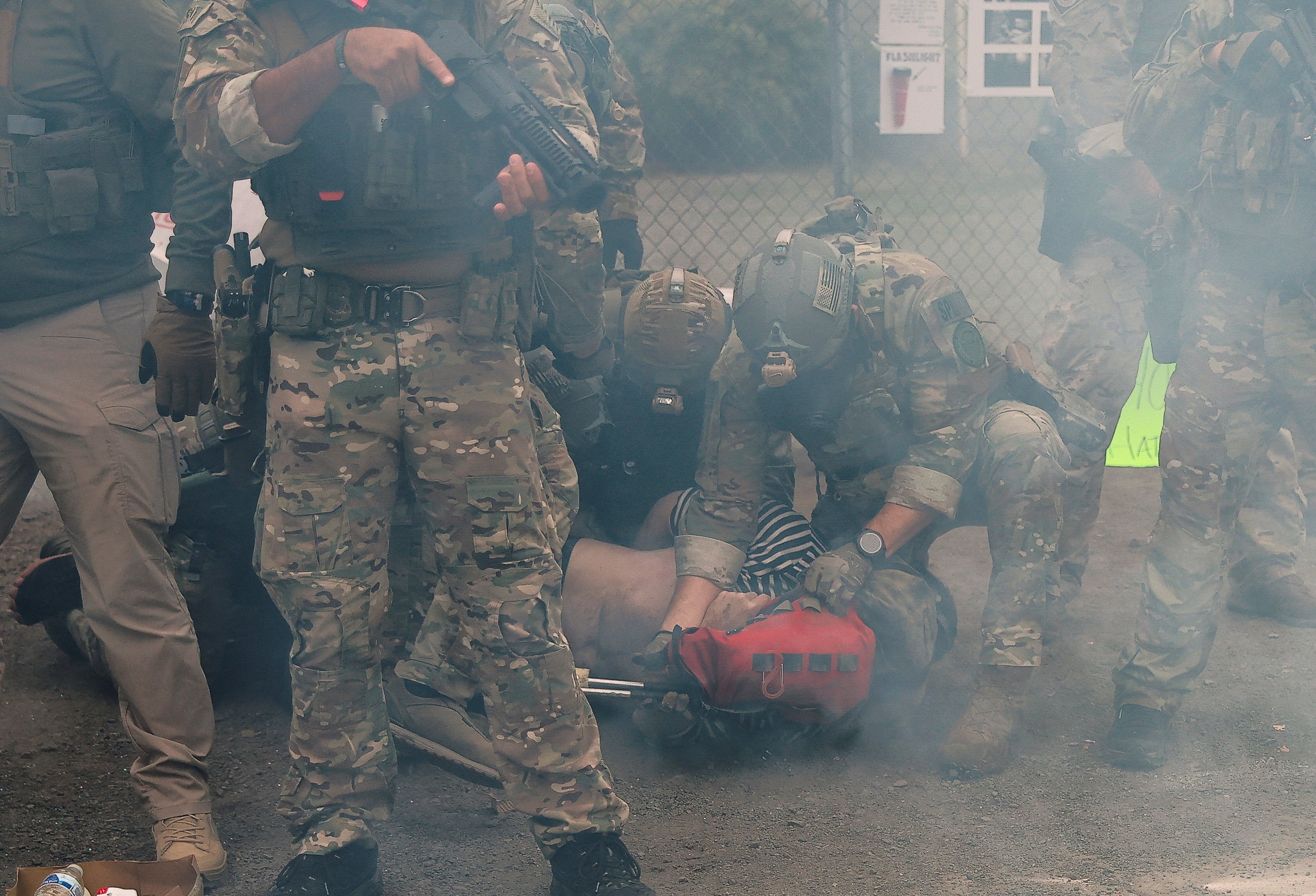 Law enforcement detains a person outside an ICE facility, amid tear gas, during a No Kings protest in Portland