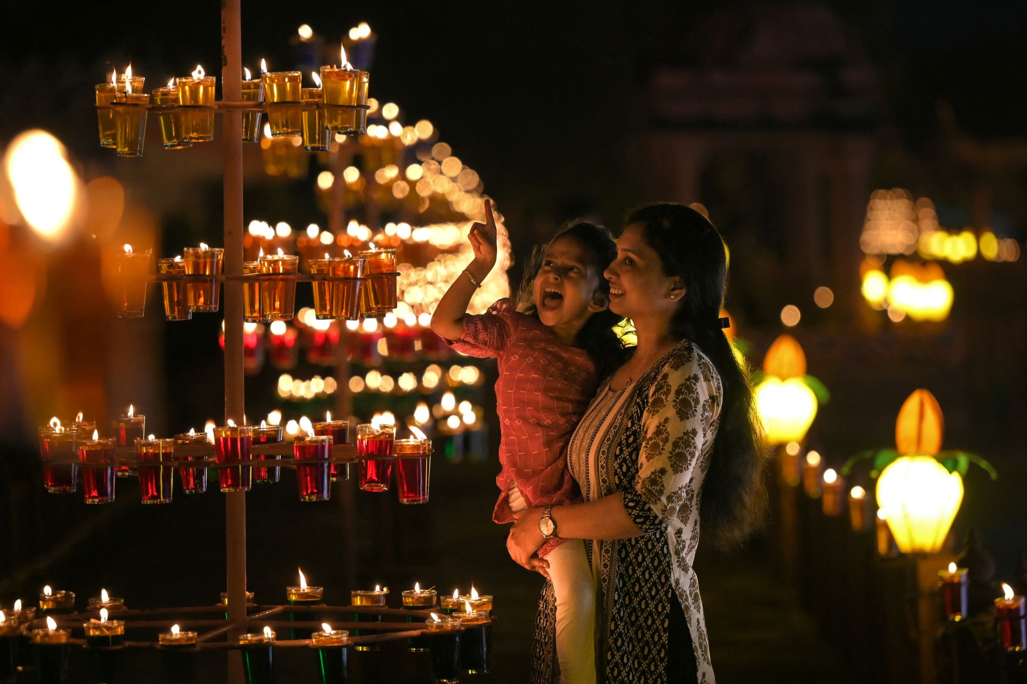 People react as they gather around the oil lamps placed outside the Akshardham Temple, on the outskirts of Ahmedabad, on 19 October 2025