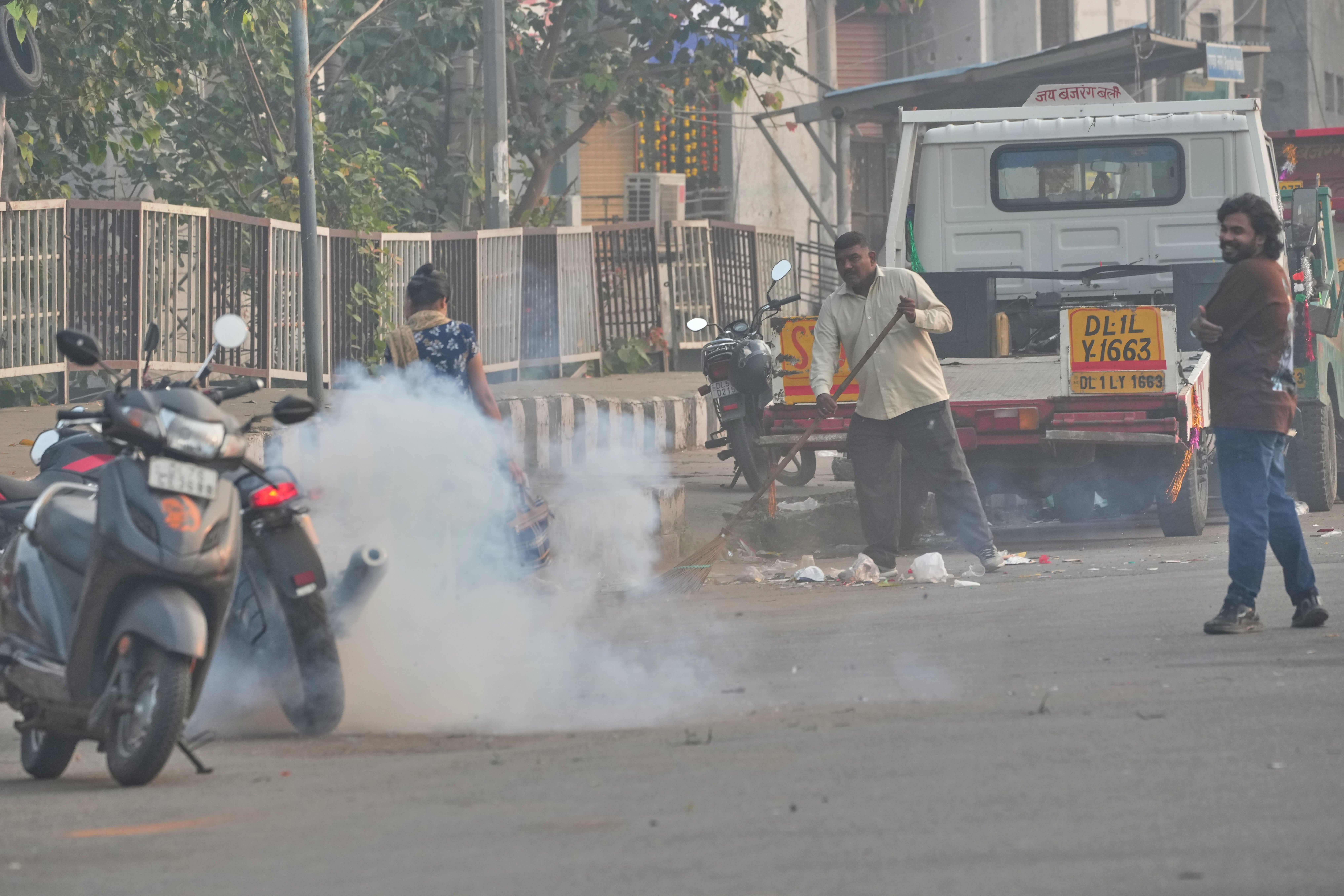 <p>A municipal worker sweeps as a person burns firecrackers amidst morning smog in New Delhi, India</p>