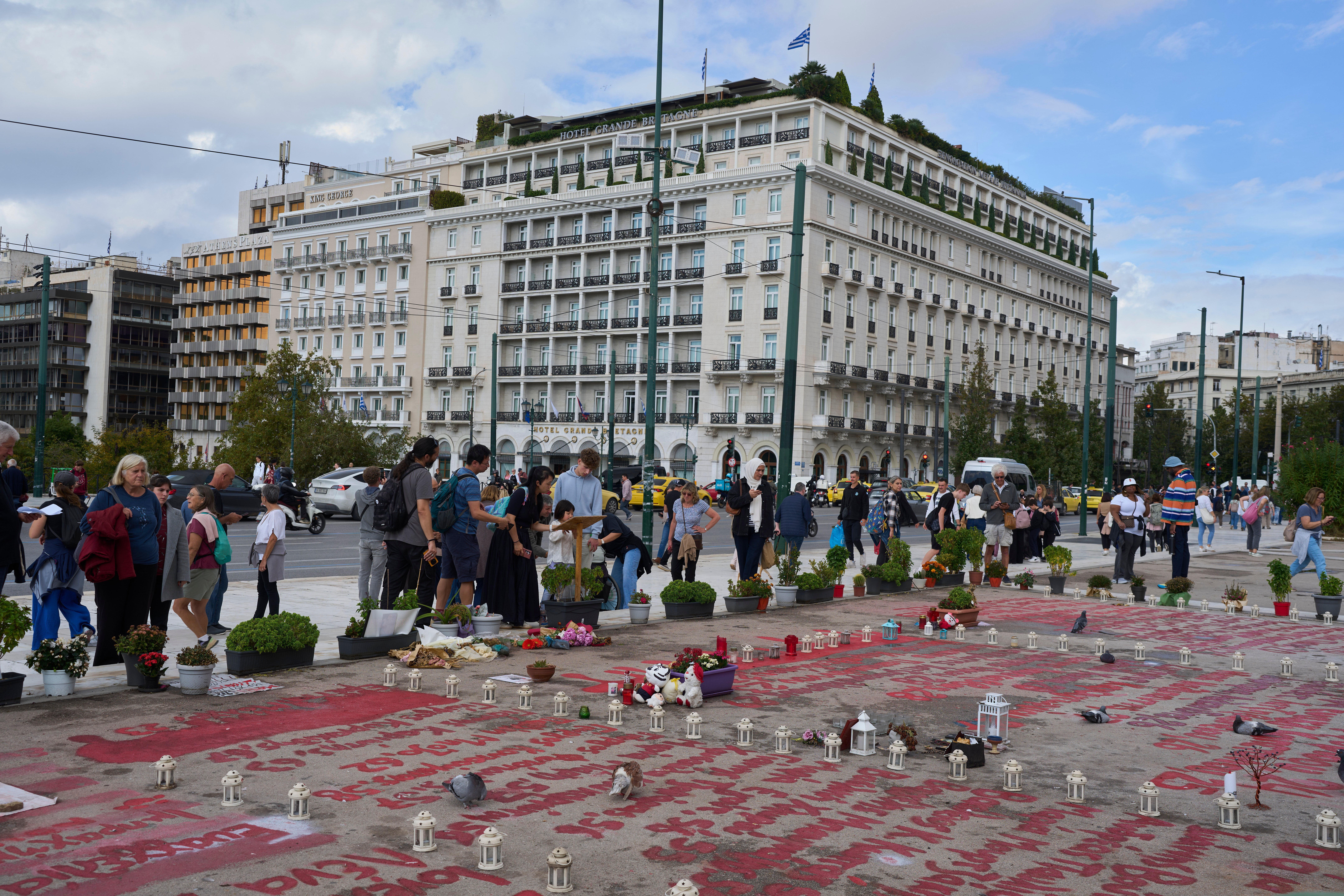 People stand in the square where the names of 57 victims of Greece's deadliest train crash are written on the ground, as Parliament debates regulations to protect the Tomb of the Unknown Soldier monument, which has recently been the focus of demonstrations by victims' relatives. (AP Photo/Petros Giannakouris)