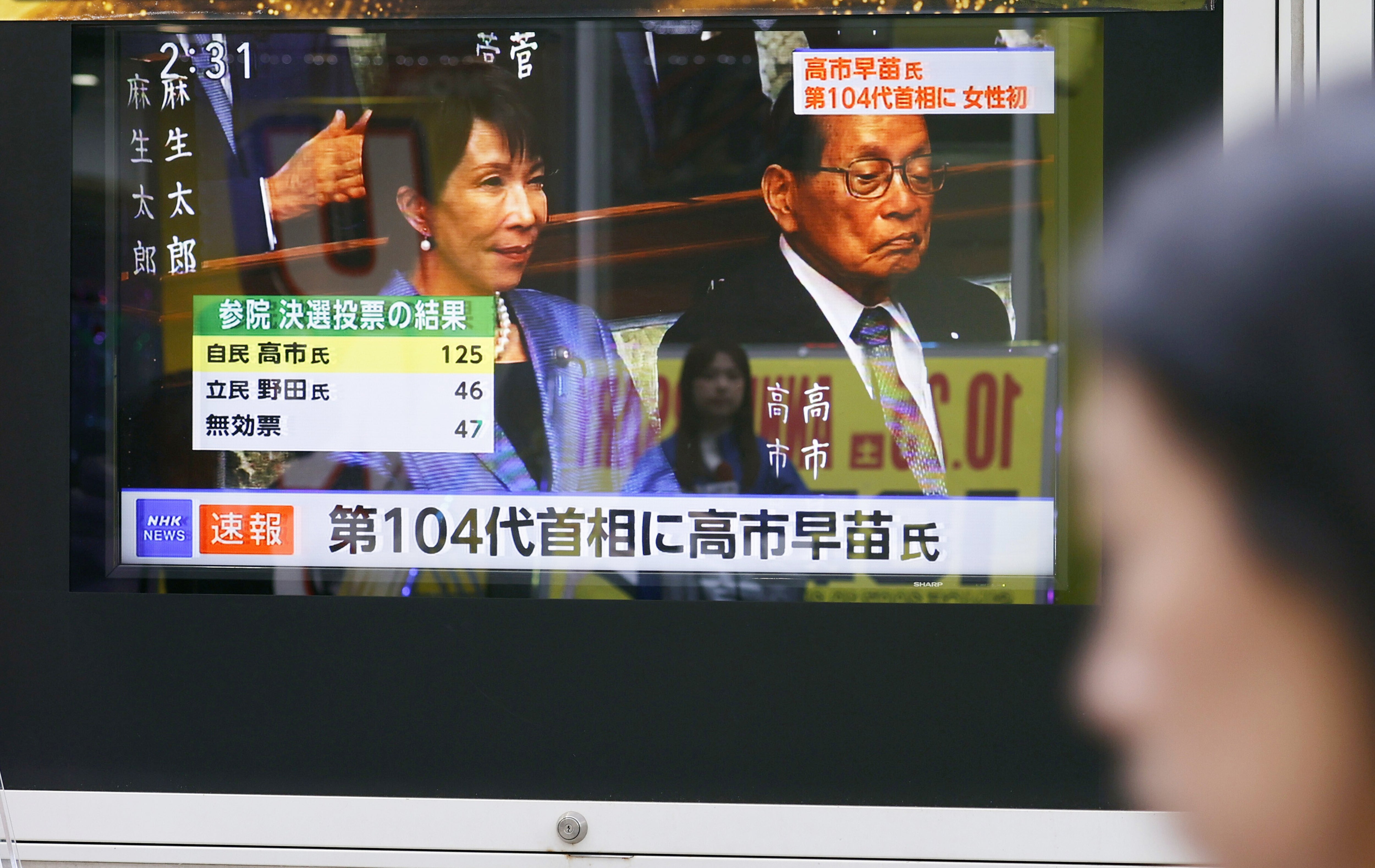 A TV monitor shows a news flash that Sanae Takaichi, left, was elected as Japan's 104th prime minister in Tokyo on Tuesday, 21 October 2025