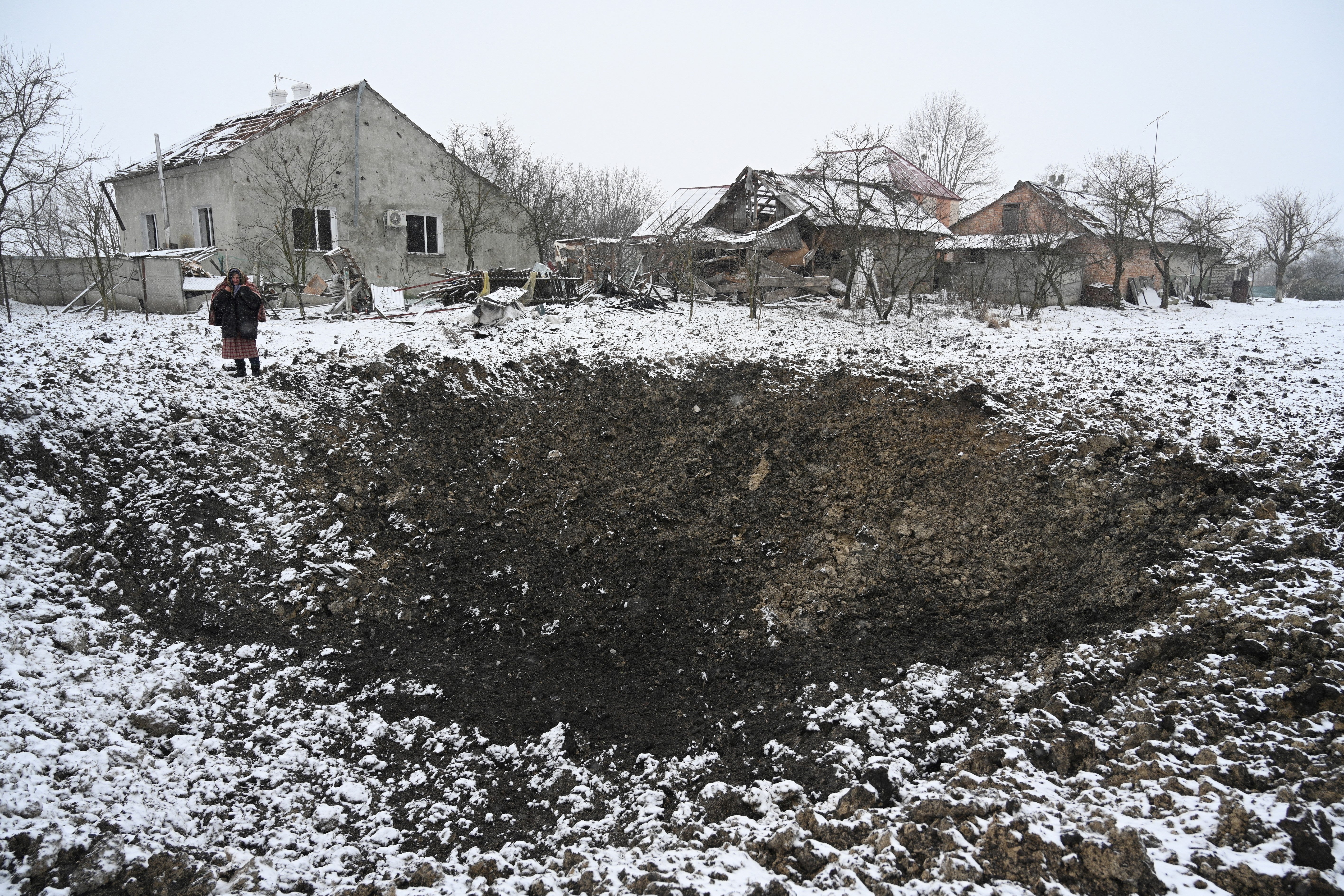 A Ukrainian villager stands next to a crater left by a Russian missile in 2022