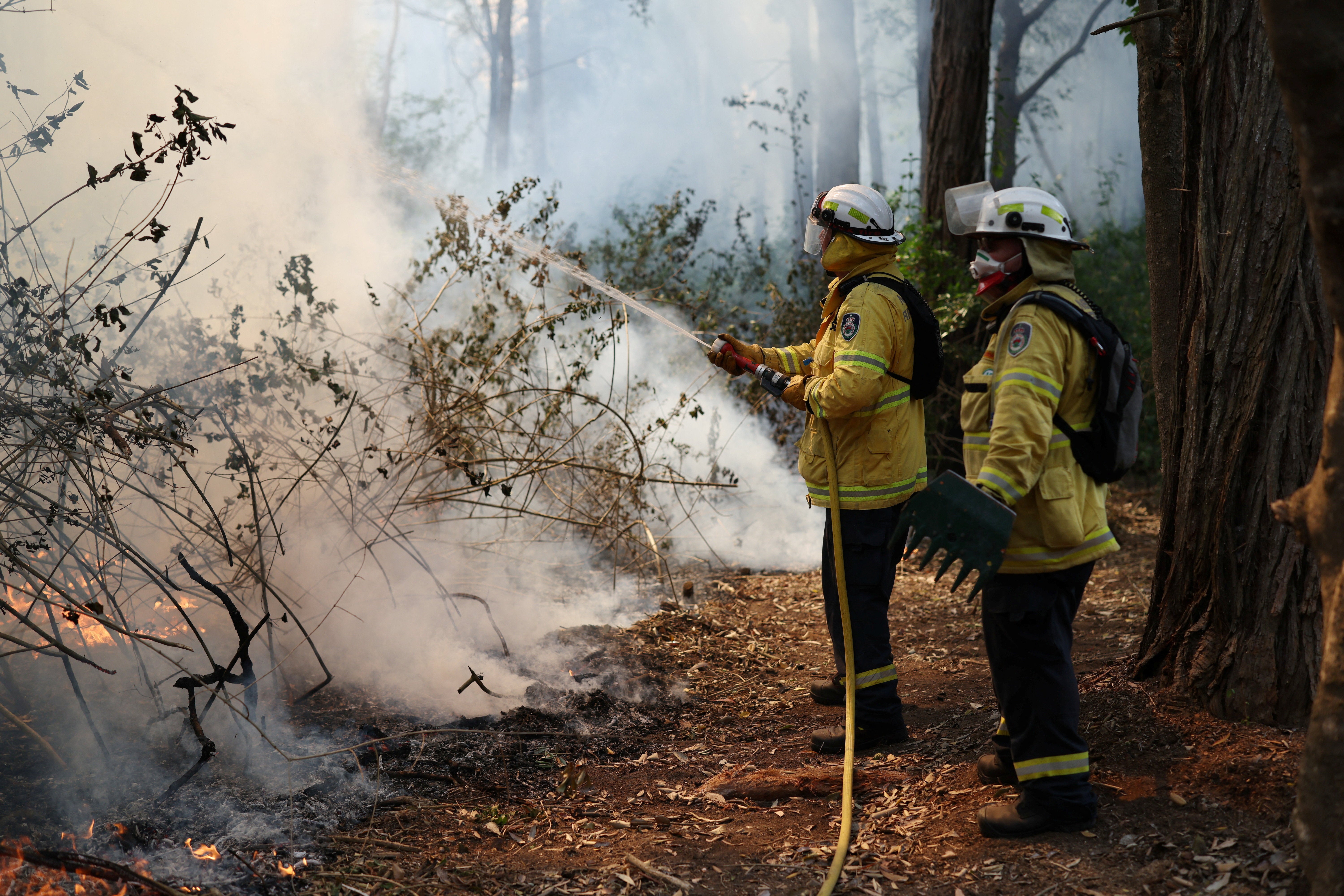 A member of the NSW Rural Fire Service holds a fire hose during a hazard reduction burn in Dural, Australia