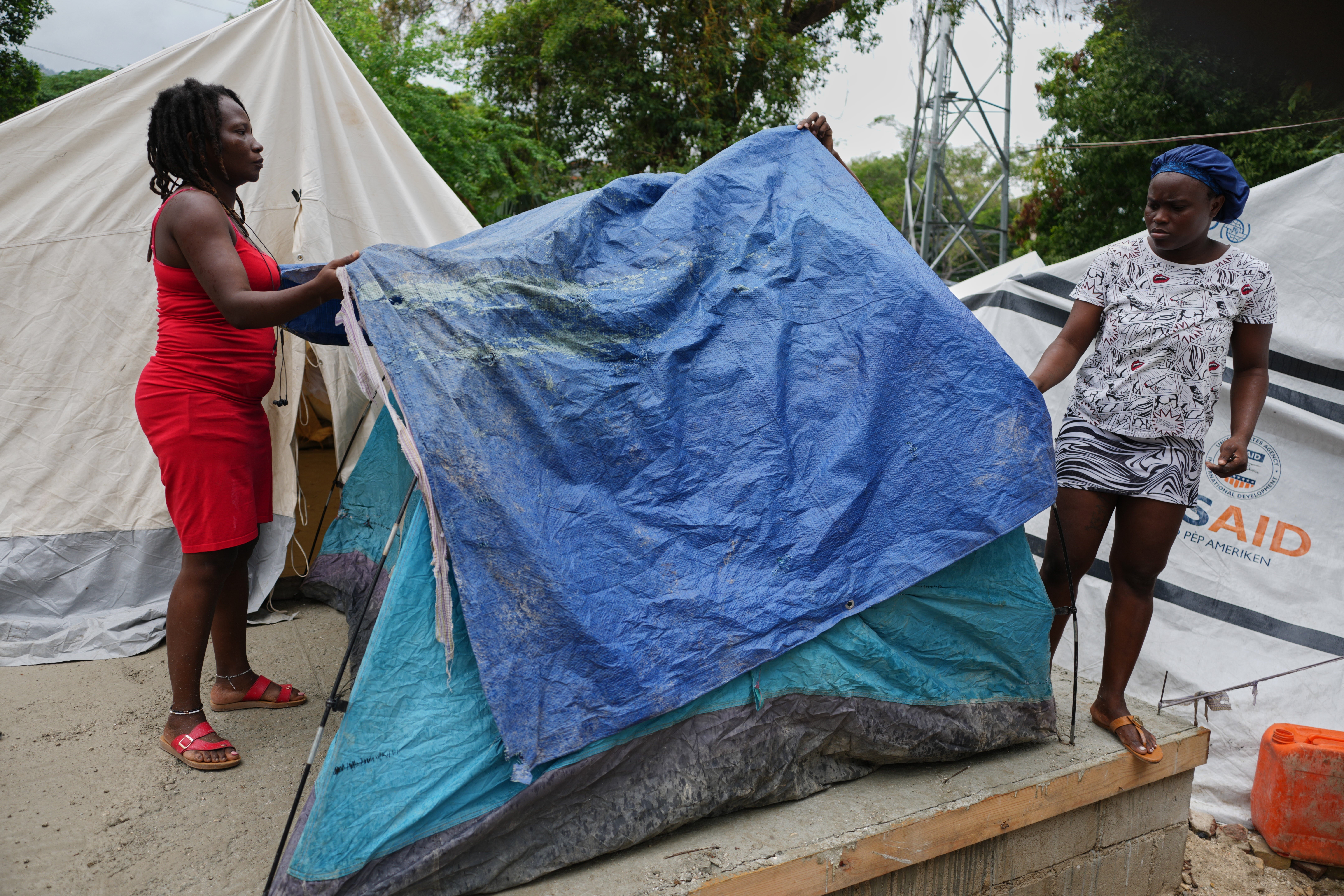 People place plastic tarps over their tents ahead of expected rain at a shelter for families displaced by gang violence in Port-au-Prince, Haiti