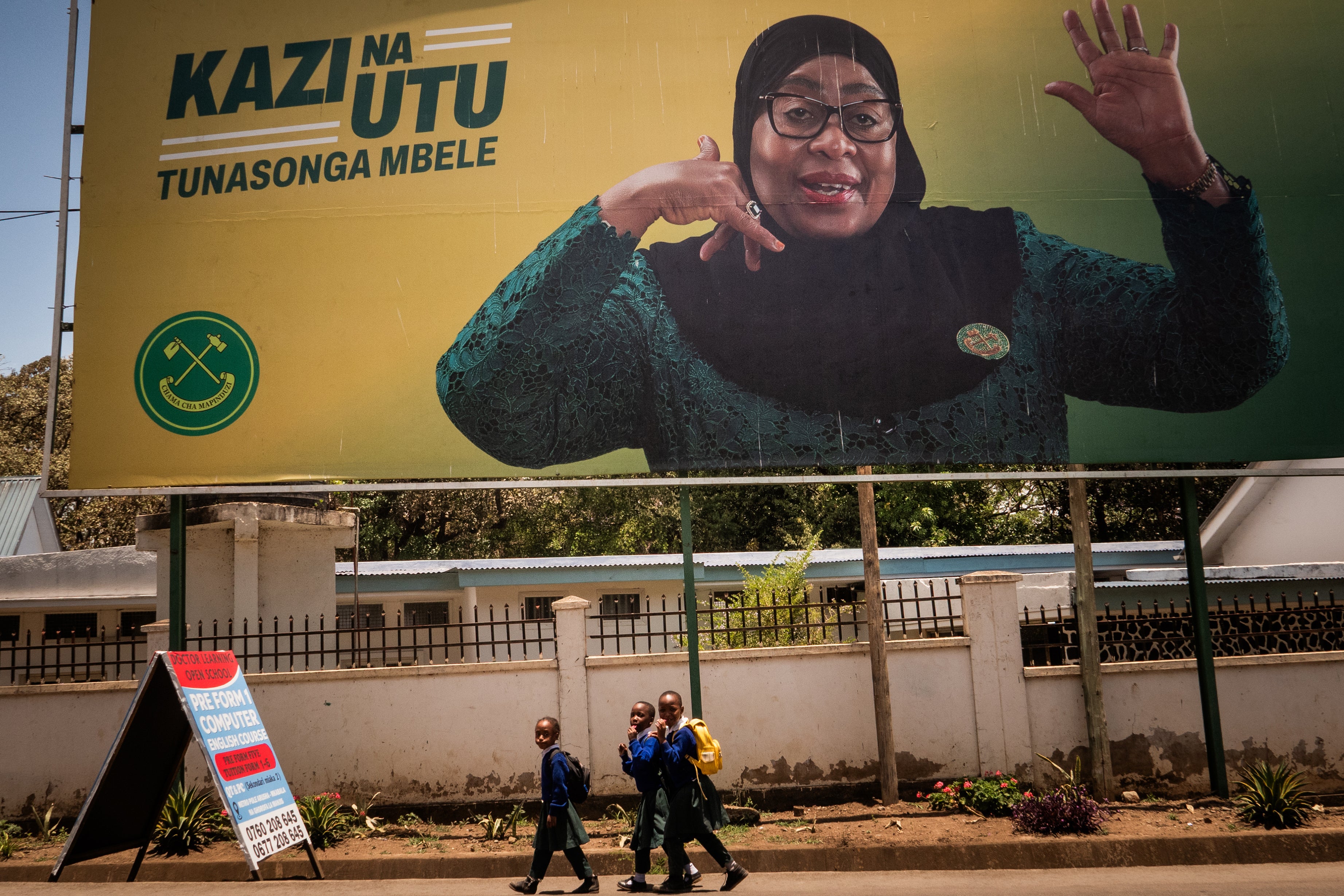 Children walk past a billboard for Tanzanian presidential candidate Samia Suluhu Hassan