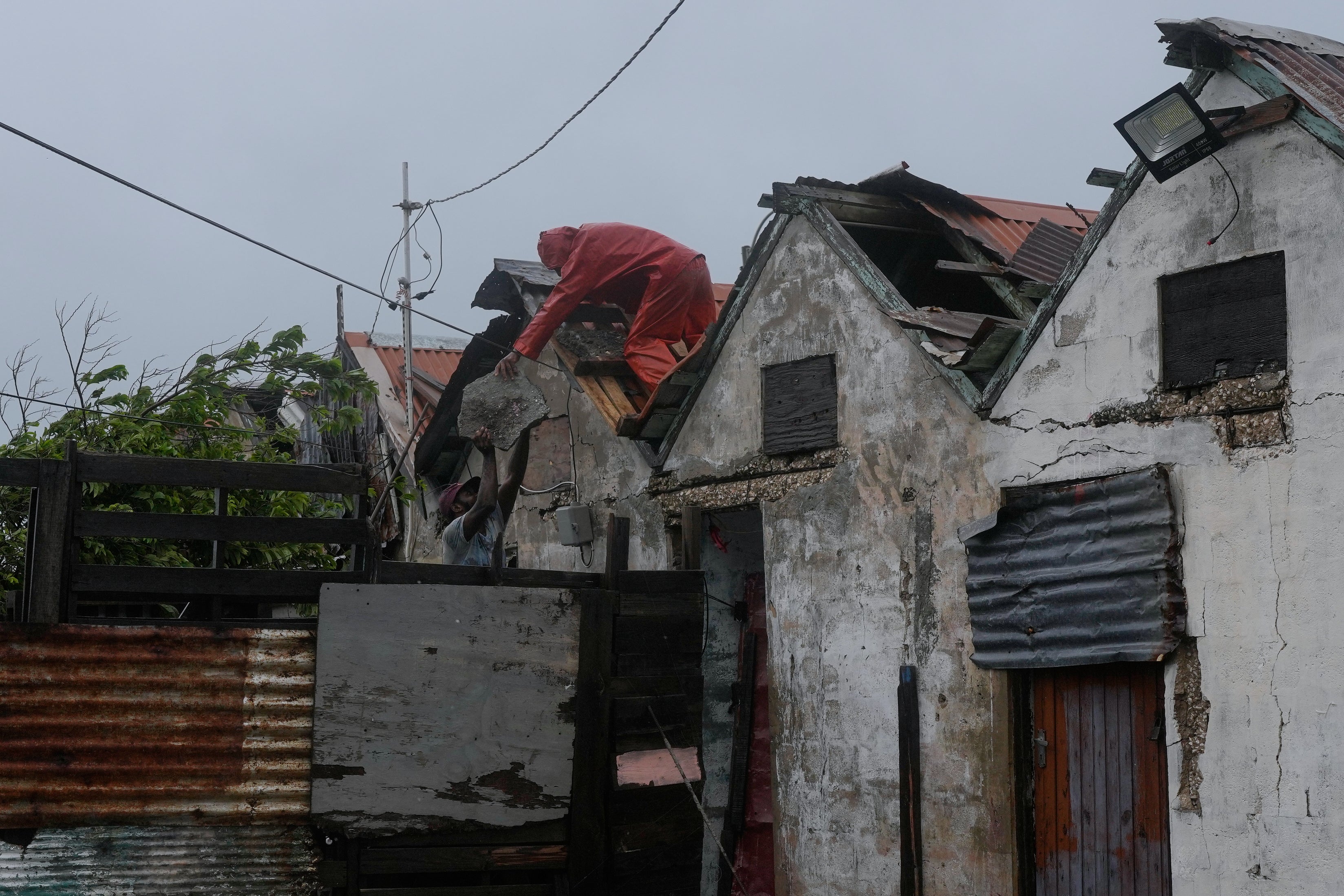 Men remove a loose section of roof in Kingston, Jamaica, in preparation for Hurricane Melissa’s devastating winds