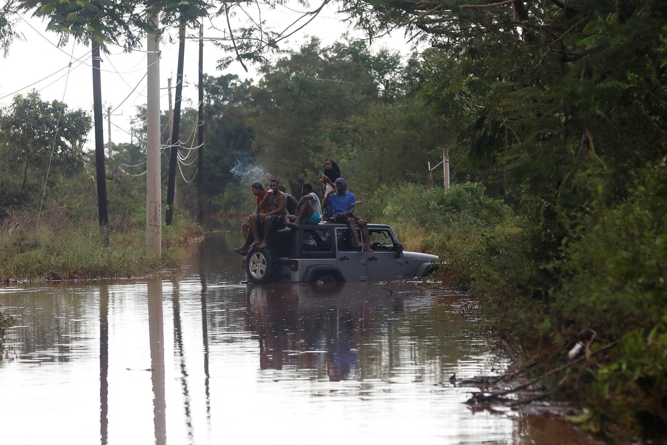 People sit on the roof of a vehicle riding on a flooded road in Prospect, Manchester, Jamaica