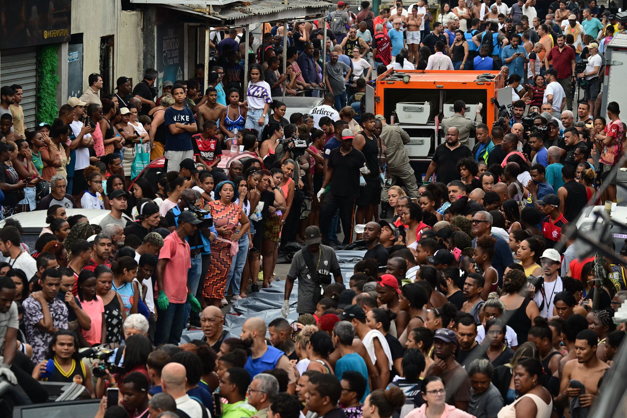 Residents stand next to lined-up bodies in front of a morgue truck on Sao Lucas Square of the Vila Cruzeiro favela at the Penha complex in Rio de Janeiro, Brazil