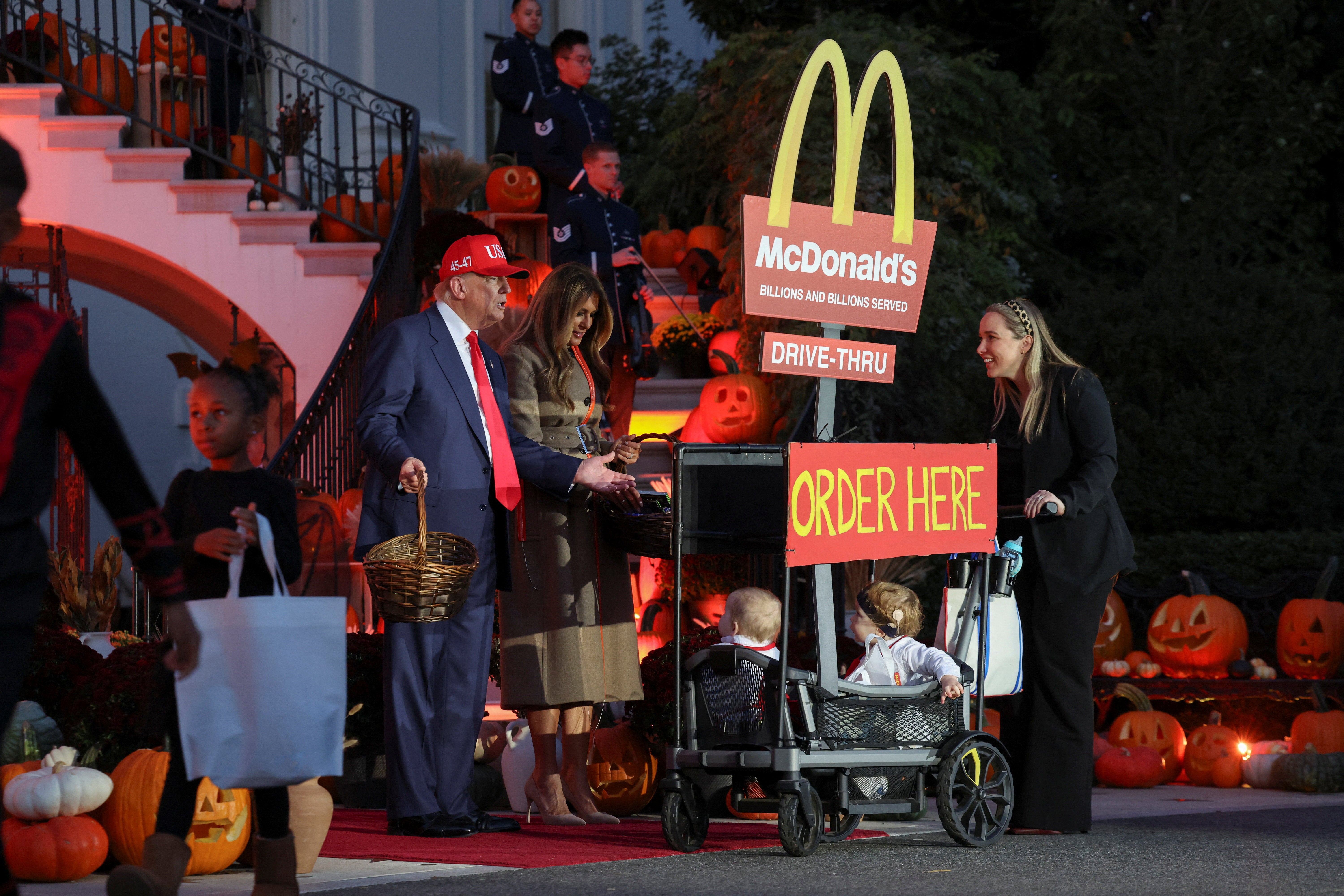 President Donald Trump and First Lady Melania Trump greet two trick-or-treaters in a wagon displaying the McDonald’s drive-thru sign at the White House Halloween event