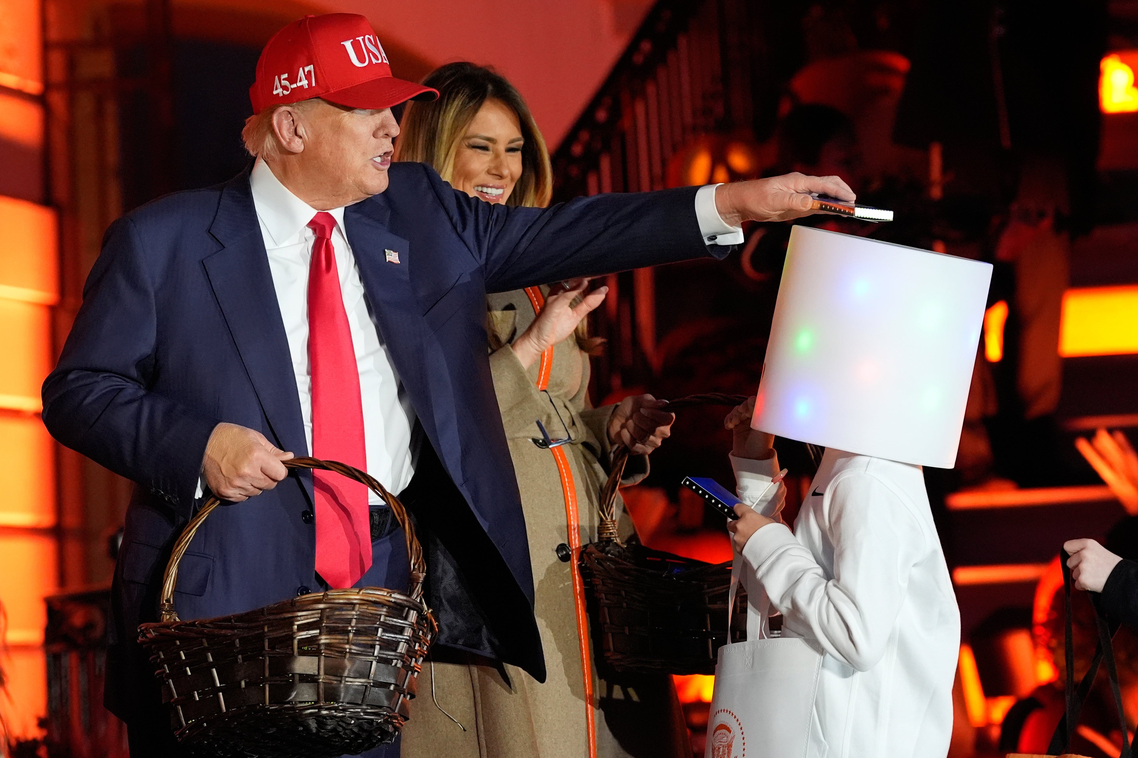 President Donald Trump places a bar of candy on top of a child’s costume at the White House Halloween event