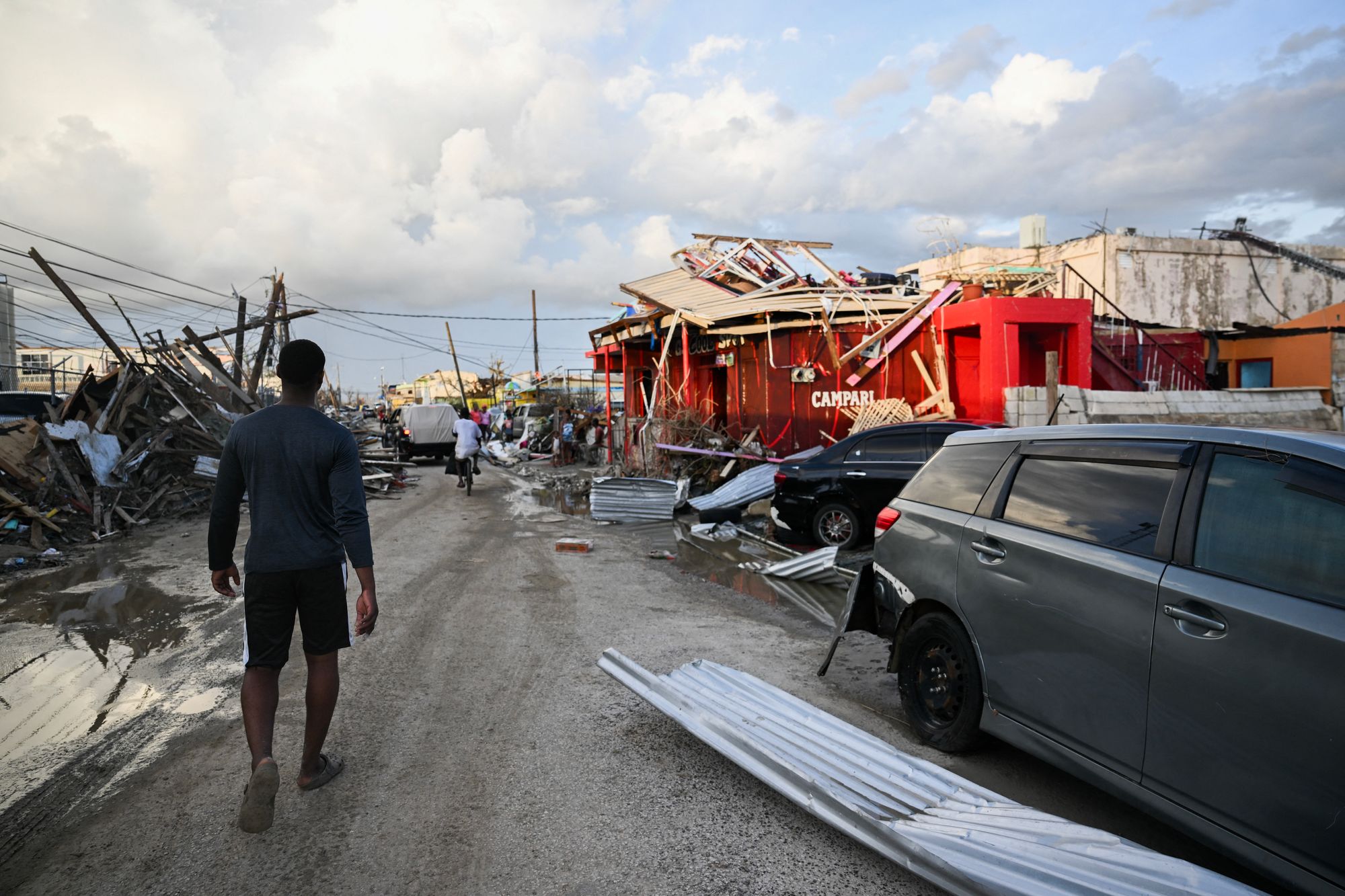 A man walks past a car and damaged buildings on Friday following the passage of Hurricane Melissa, in Black River, Jamaica. The hurricane has been cited in the deaths of dozens of people there in Cuba and Haiti