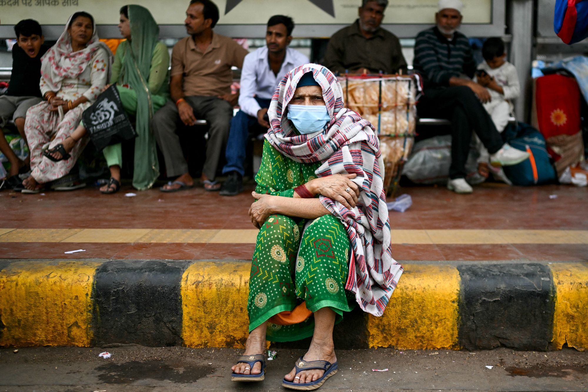 <p>An elderly lady wearing a mask sits along a road amid smoggy conditions in Delhi on 30 October 2025</p>