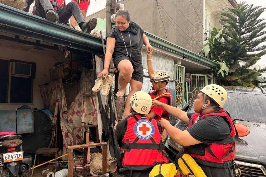 In this photo provided by the Philippine Red Cross, the Water Search and Rescue Team assists individuals trapped on a roof in the Talamban barangay of Cebu