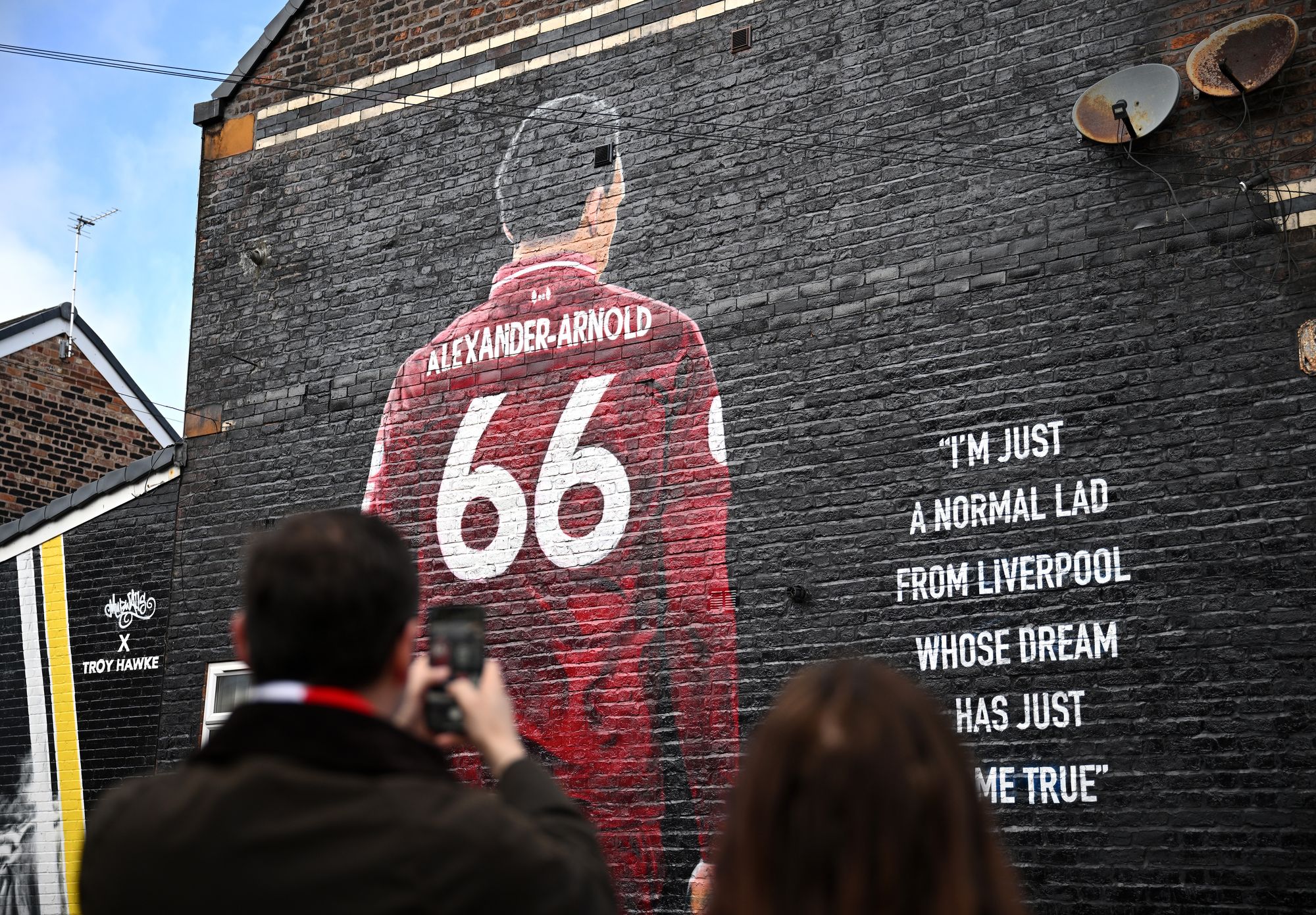 Fans of Liverpool take a picture of a mural which features Trent Alexander-Arnold before it was vandalised