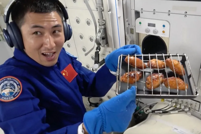<p>Chinese astronaut Wu Fei holds a rack of chicken wings prepared in the new space oven</p>