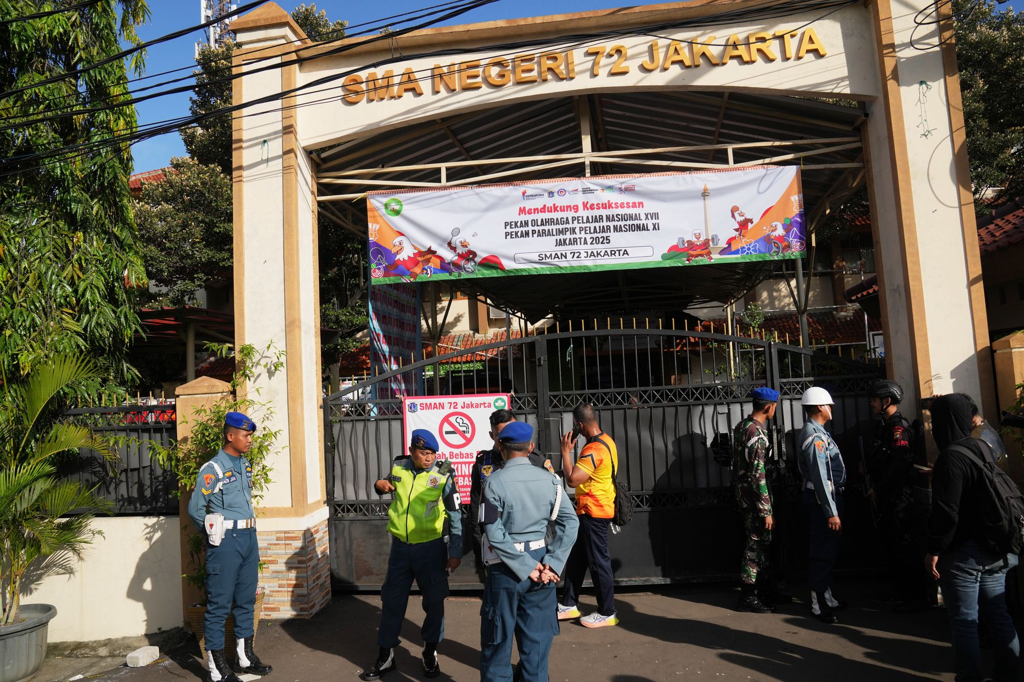 Police officers and military personnel stand guard at the gate of a school where explosions occurred in Jakarta