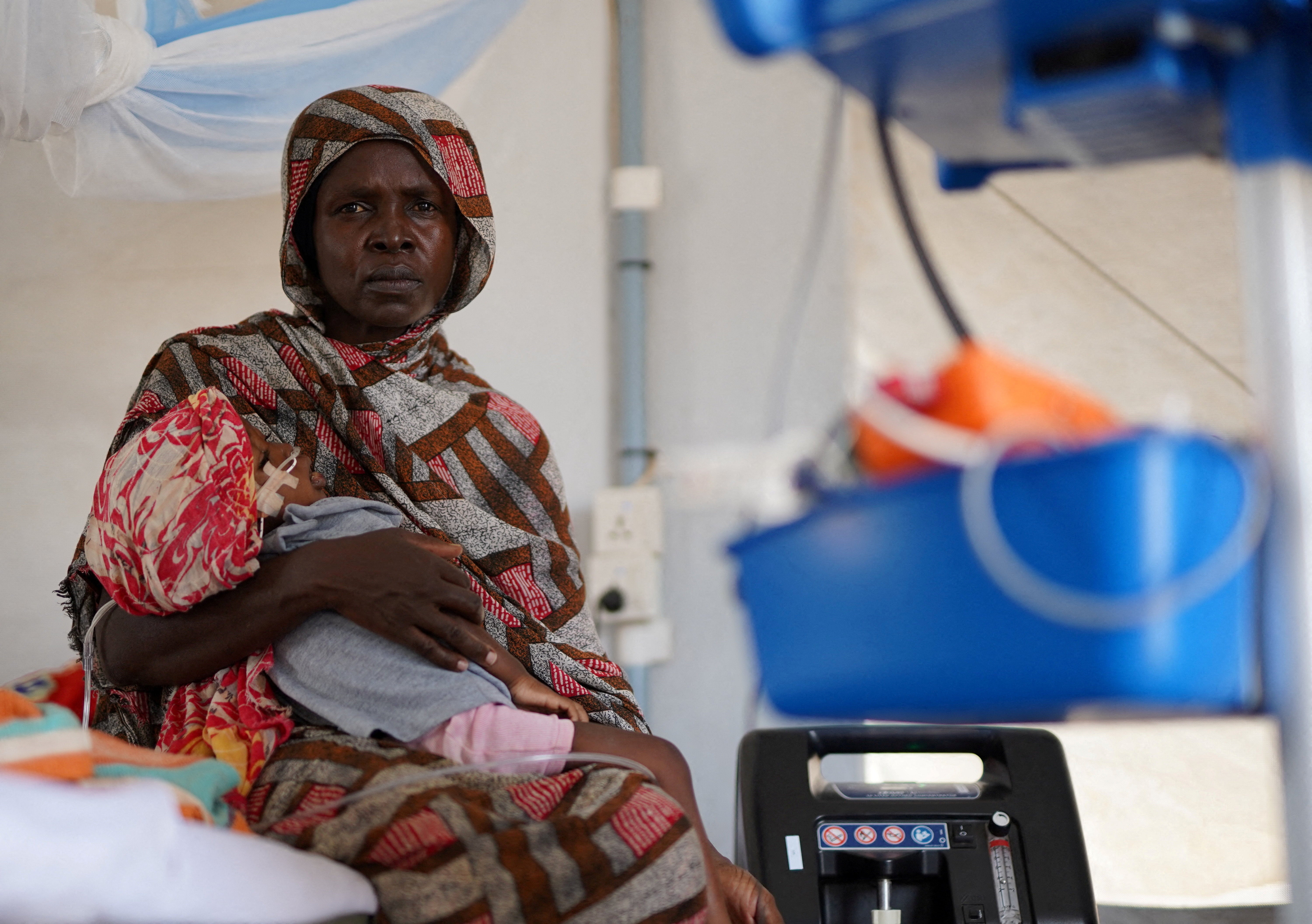 An injured displaced Sudanese woman who fled violence in el-Fasher receives treatment while carrying her child at a makeshift clinic run by Medecins Sans Frontieres